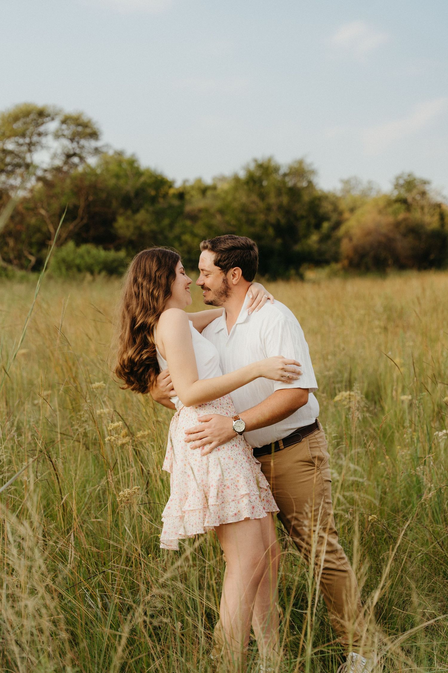 Romantic couple embracing and almost kissing in a golden sunlit field at the Pretoria Botanical Gardens at sunset.