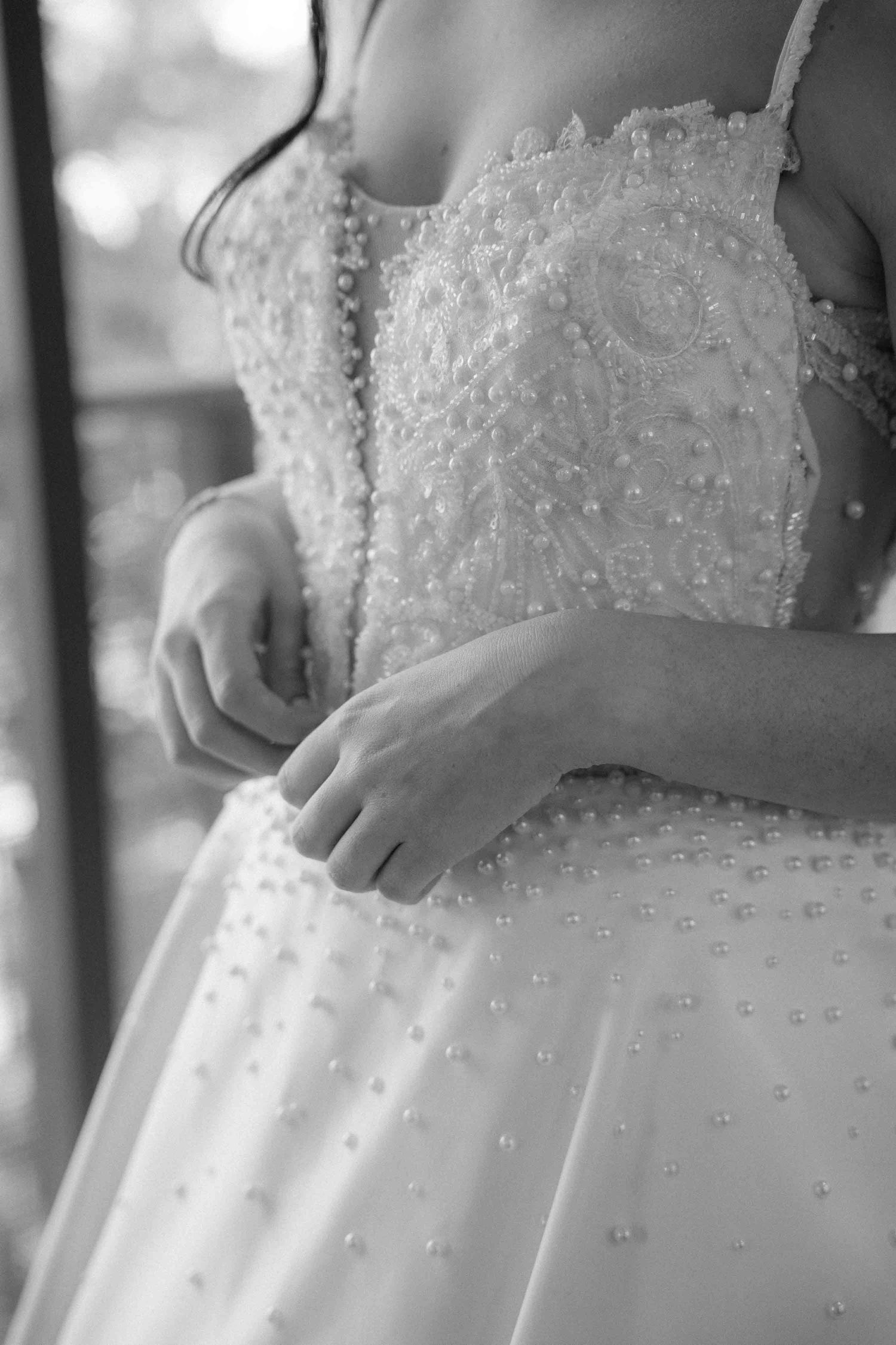 Black and white photo of a bride in a pearl-embellished wedding gown with delicate spaghetti straps and intricate beading.