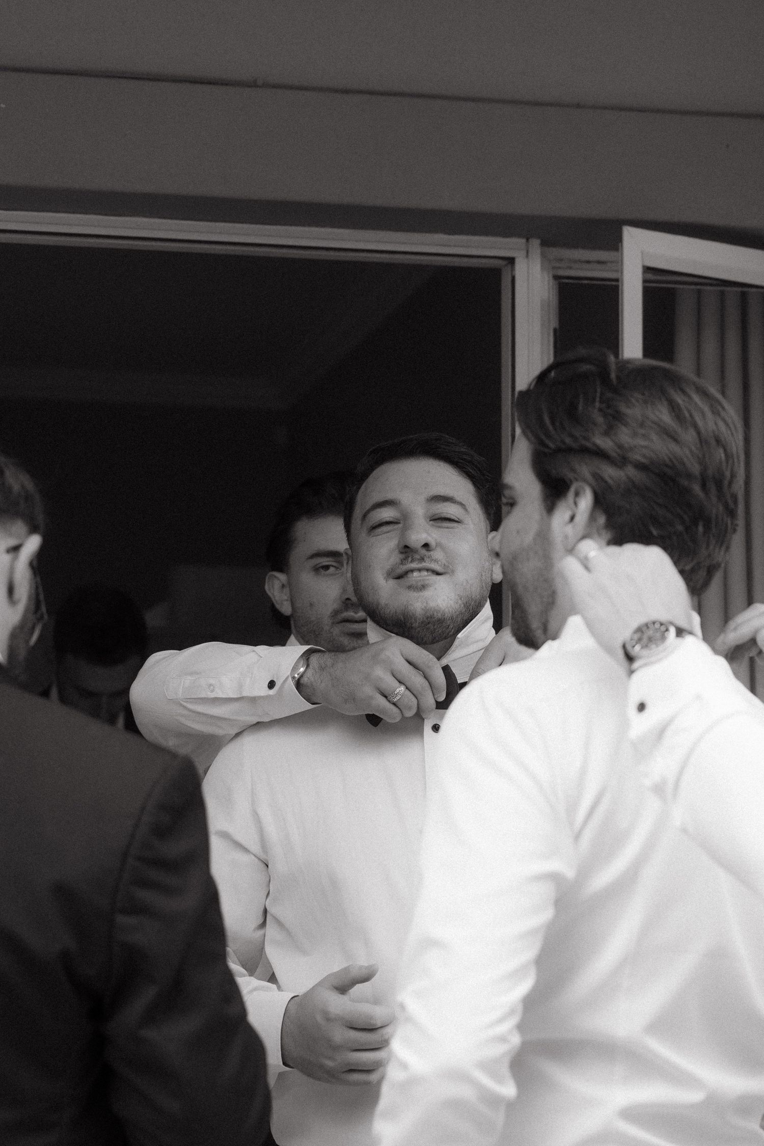 Black and white photo of groomsmen helping each other get dressed before a Johannesburg  wedding ceremony.