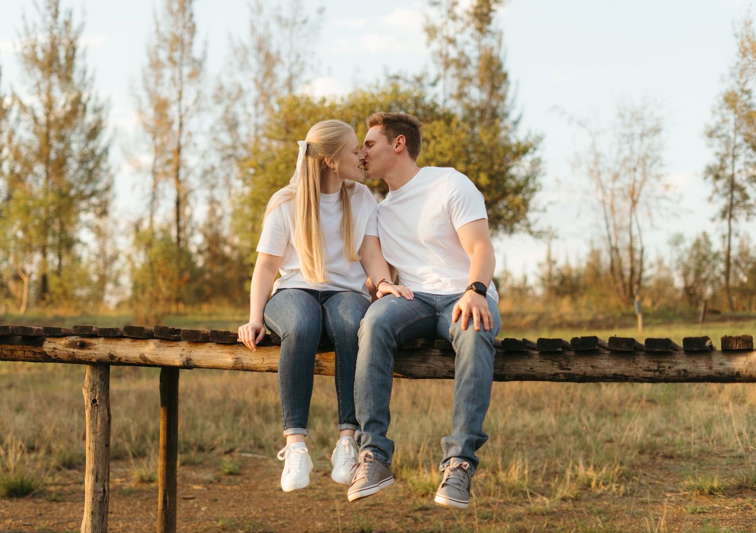 A couple shares a tender moment while sitting together on a rustic wooden bench in a scenic outdoor setting at sunset.