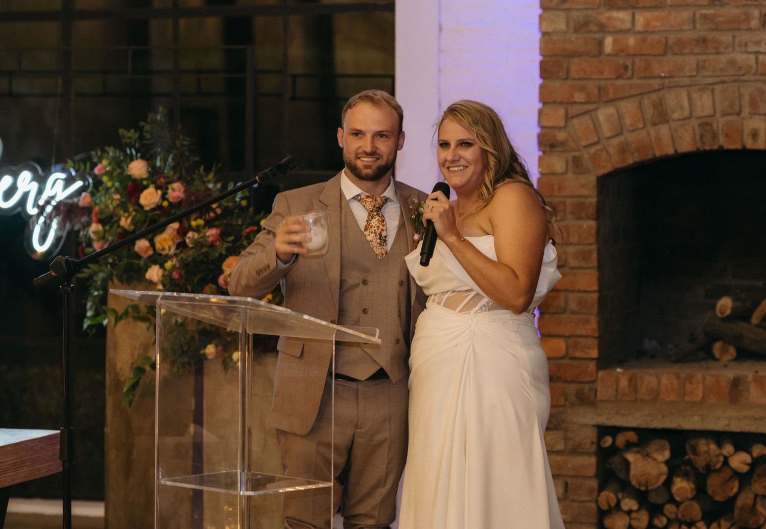 A couple shares a joyful moment during their wedding speech in front of a rustic brick wall.
