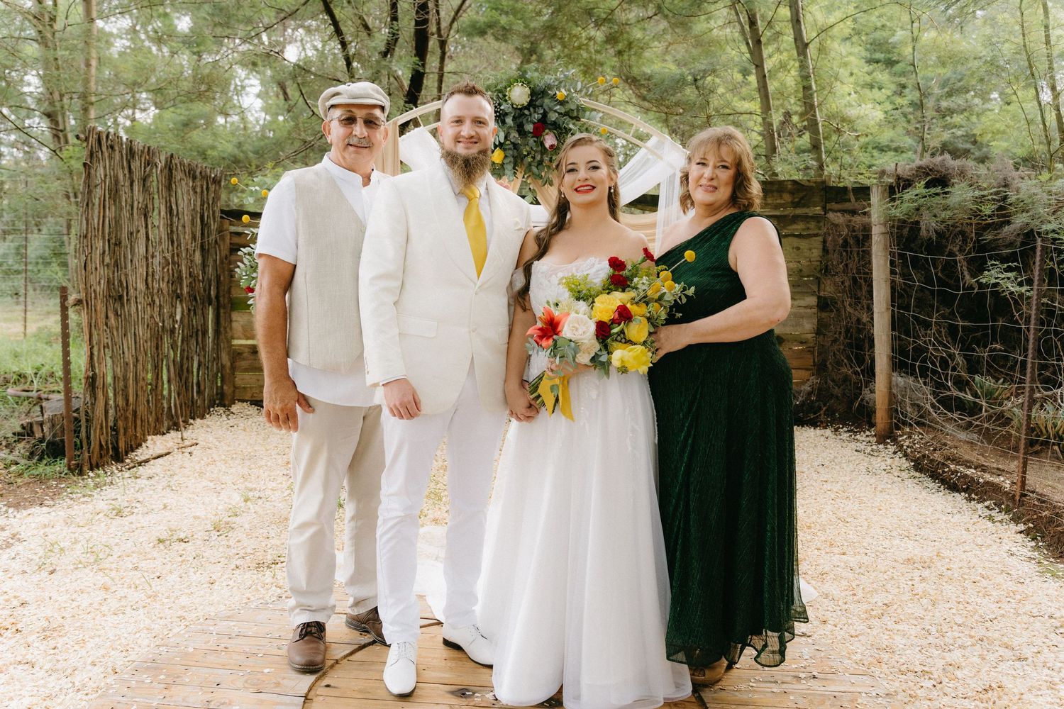 Wedding party group photo on forest path with people dressed in white and dark green attire.