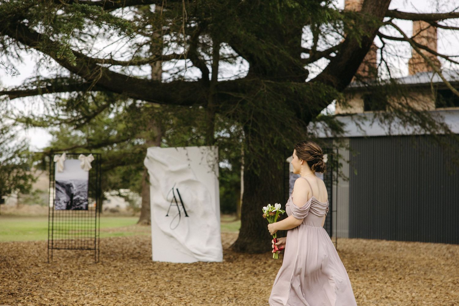 A person in a flowing dress walks past a large tree with hanging decorations outdoors.