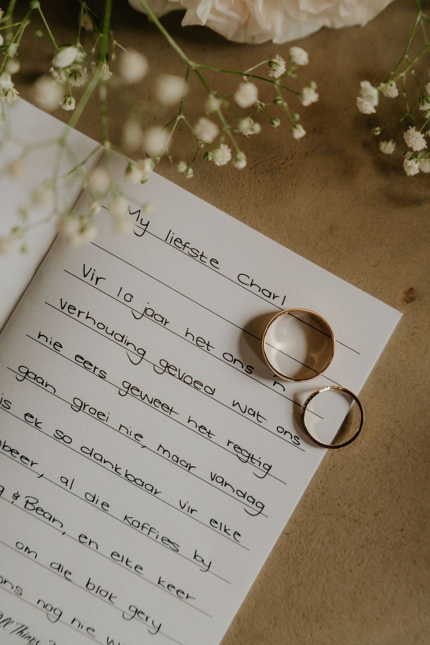 Wedding rings displayed on handwritten vows with delicate baby's breath flowers in the background.