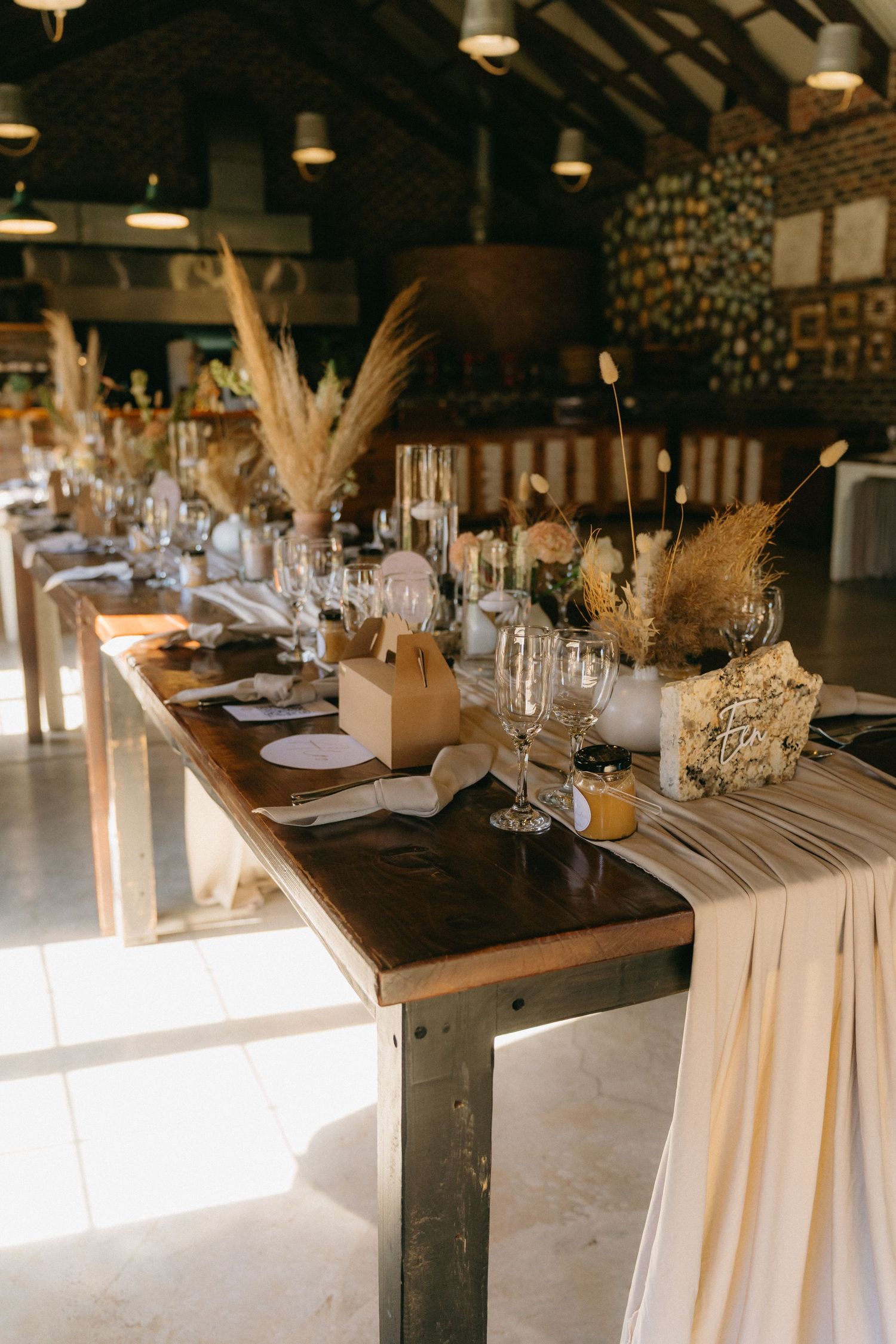 Rustic wedding reception table setting with pampas grass centerpieces and flowing white linens.