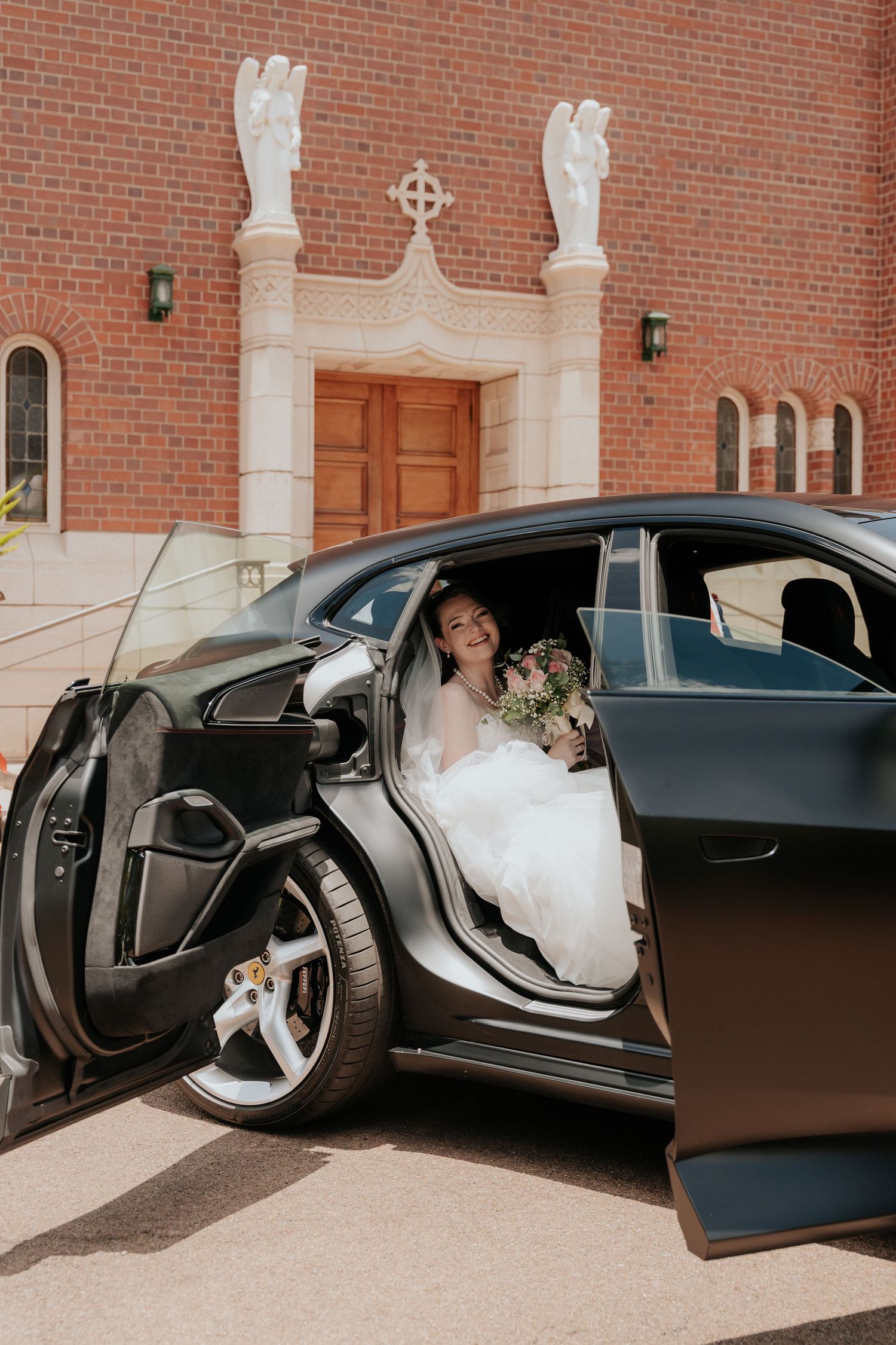 A bride in a white wedding dress emerges from a black luxury car outside Nazareth House Chapel