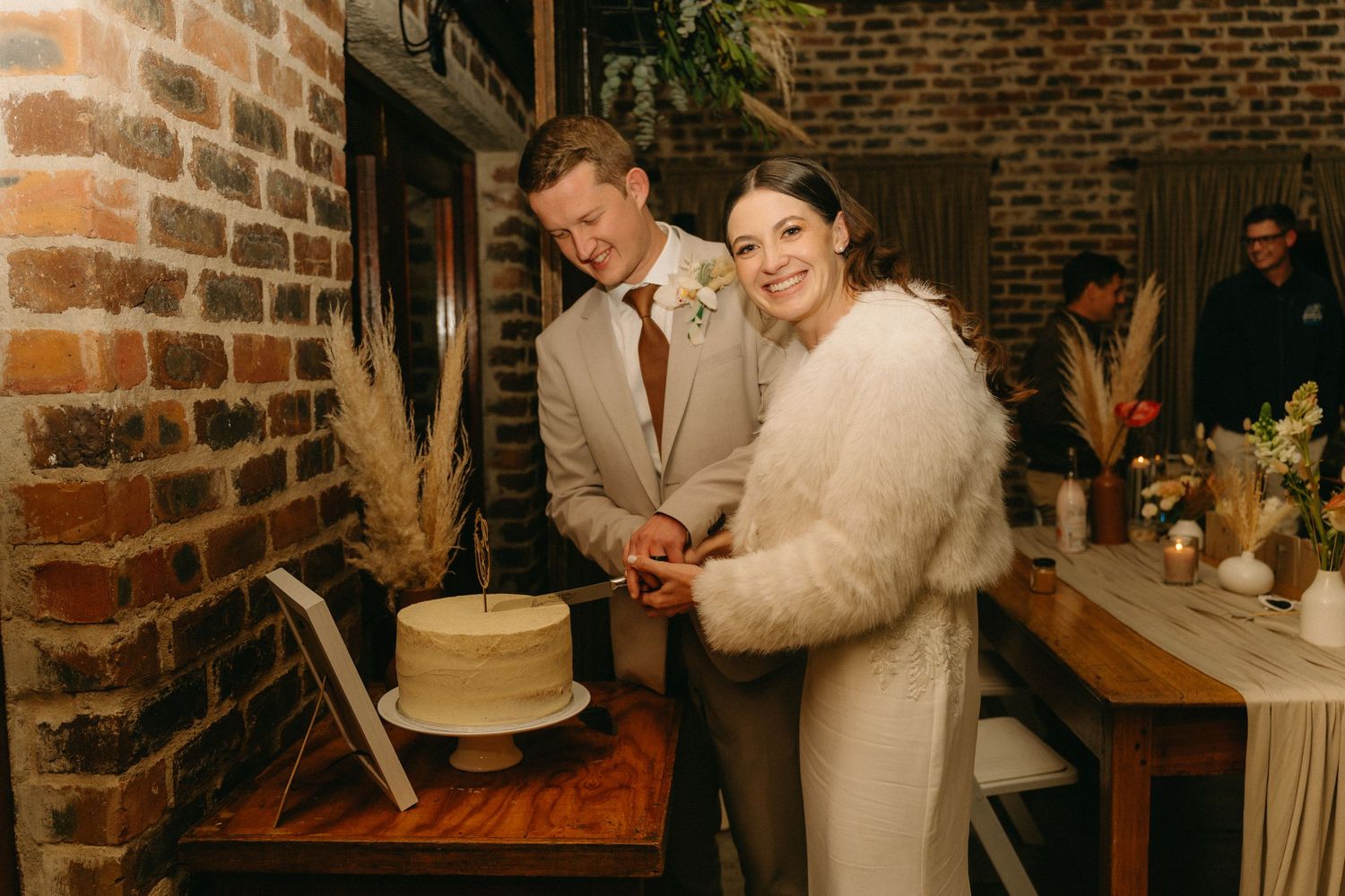 A couple cuts their wedding cake together at a rustic brick venue.