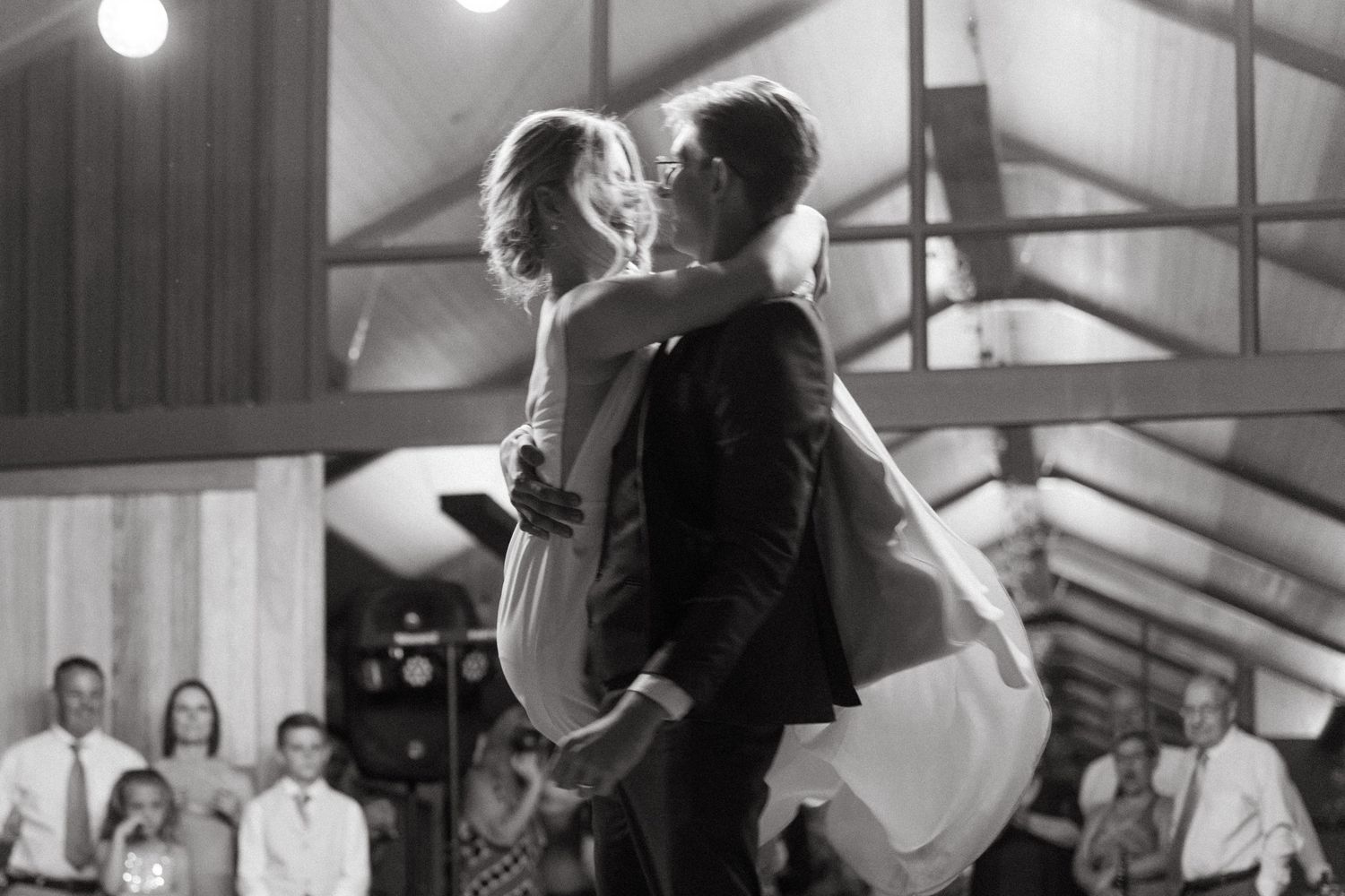A couple shares their first dance as newlyweds during a wedding reception in a rustic venue with exposed beams.