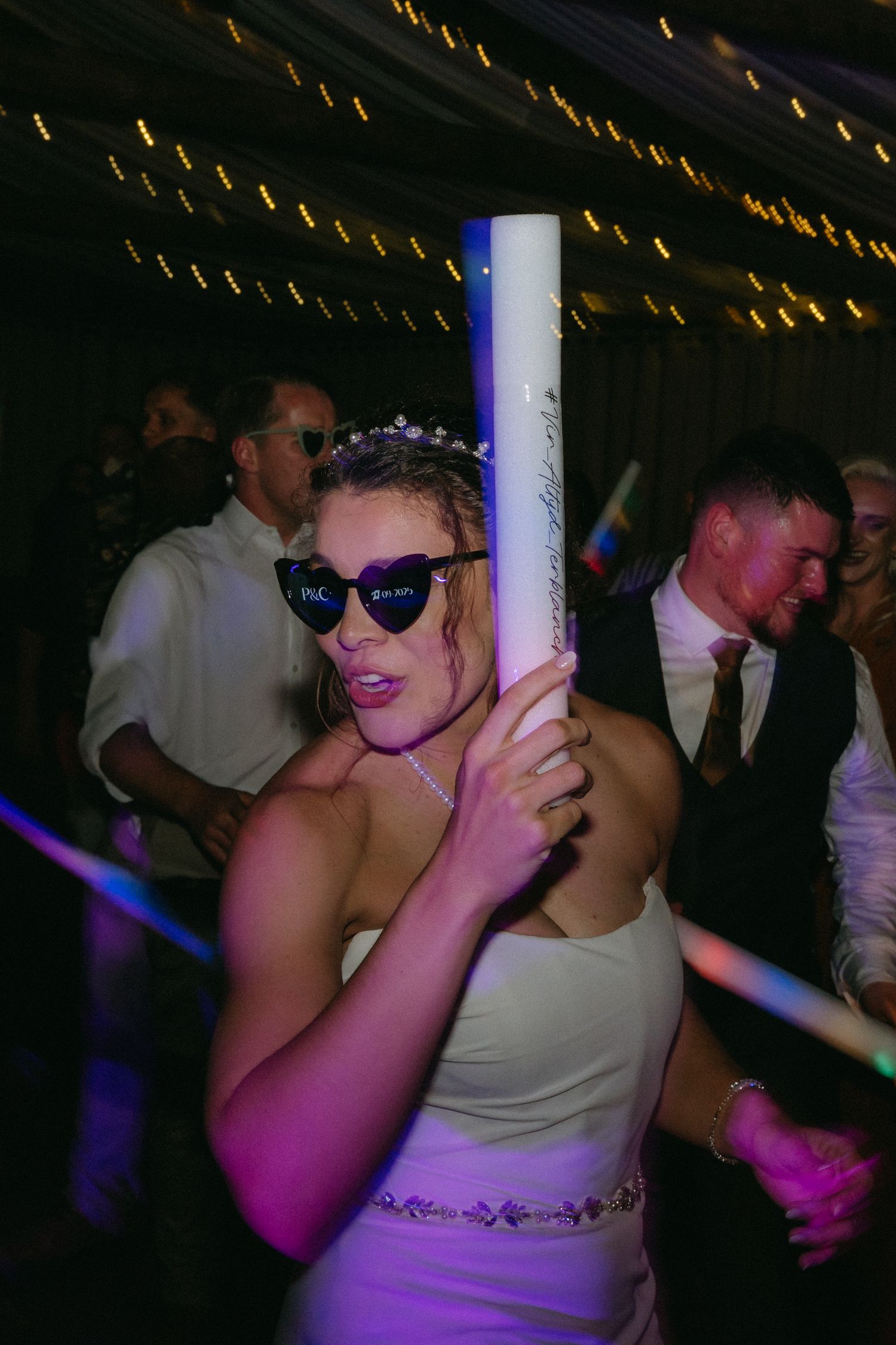 Bride dancing and enjoying herself at a wedding reception under twinkling lights.