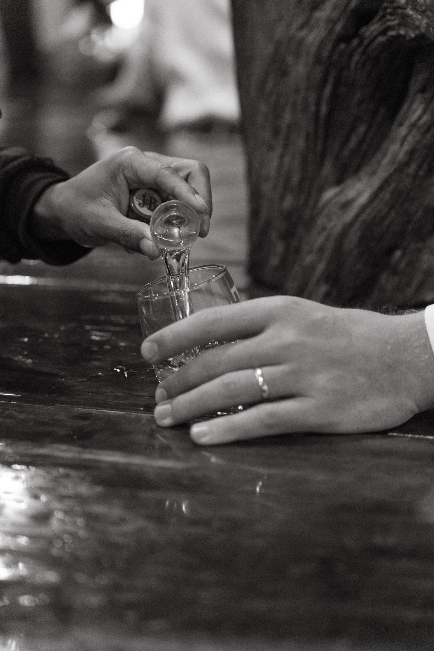 A series of black and white photos showing hands pouring liquid into small shot glasses on a reflective surface.
