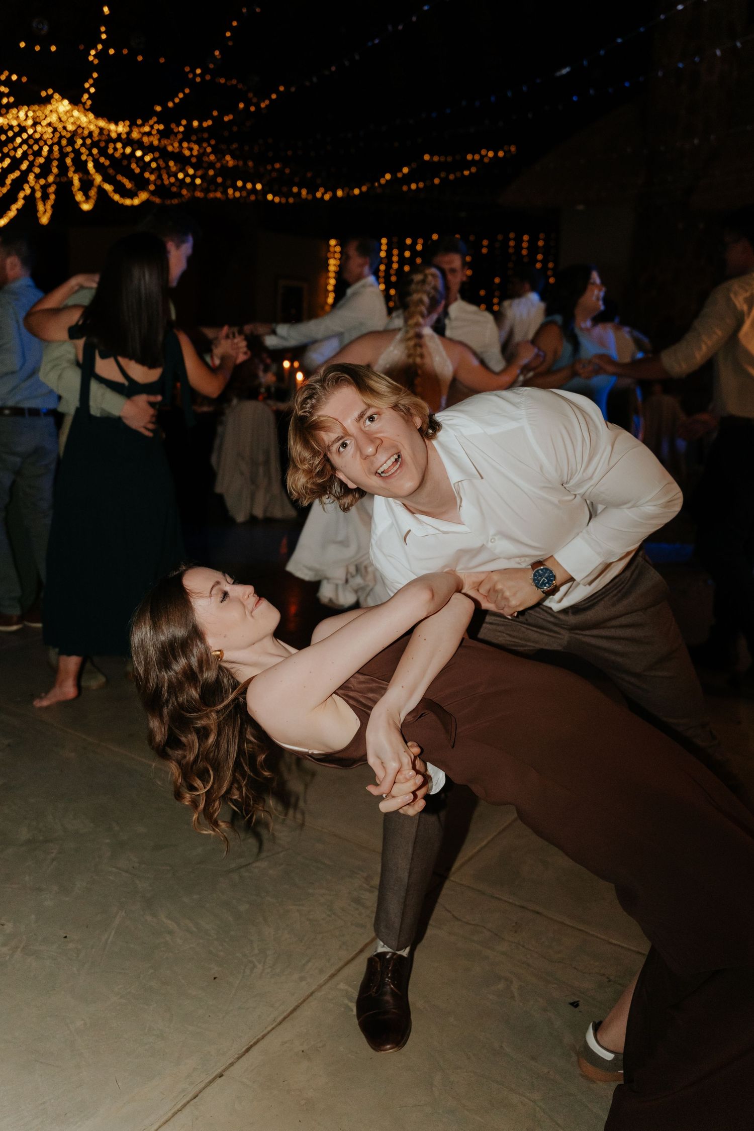Couples dancing and dipping dramatically under string lights at a wedding reception.