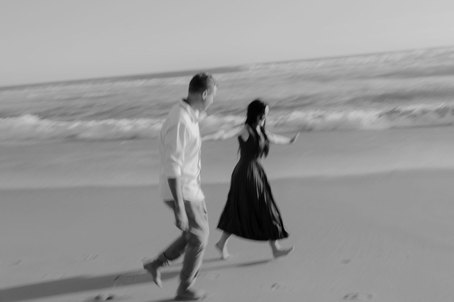 A couple walks hand in hand along a misty beach shoreline in the Western Cape in black and white.