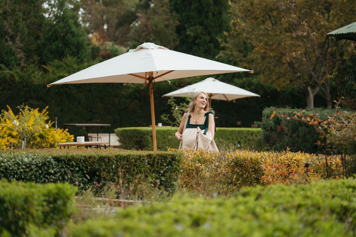 Woman walking through a manicured garden with large white patio umbrellas and lush green hedges.