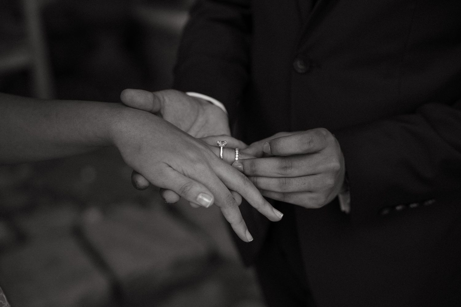 Black and white photo of groom placing wedding ring on bride's finger during ceremony.