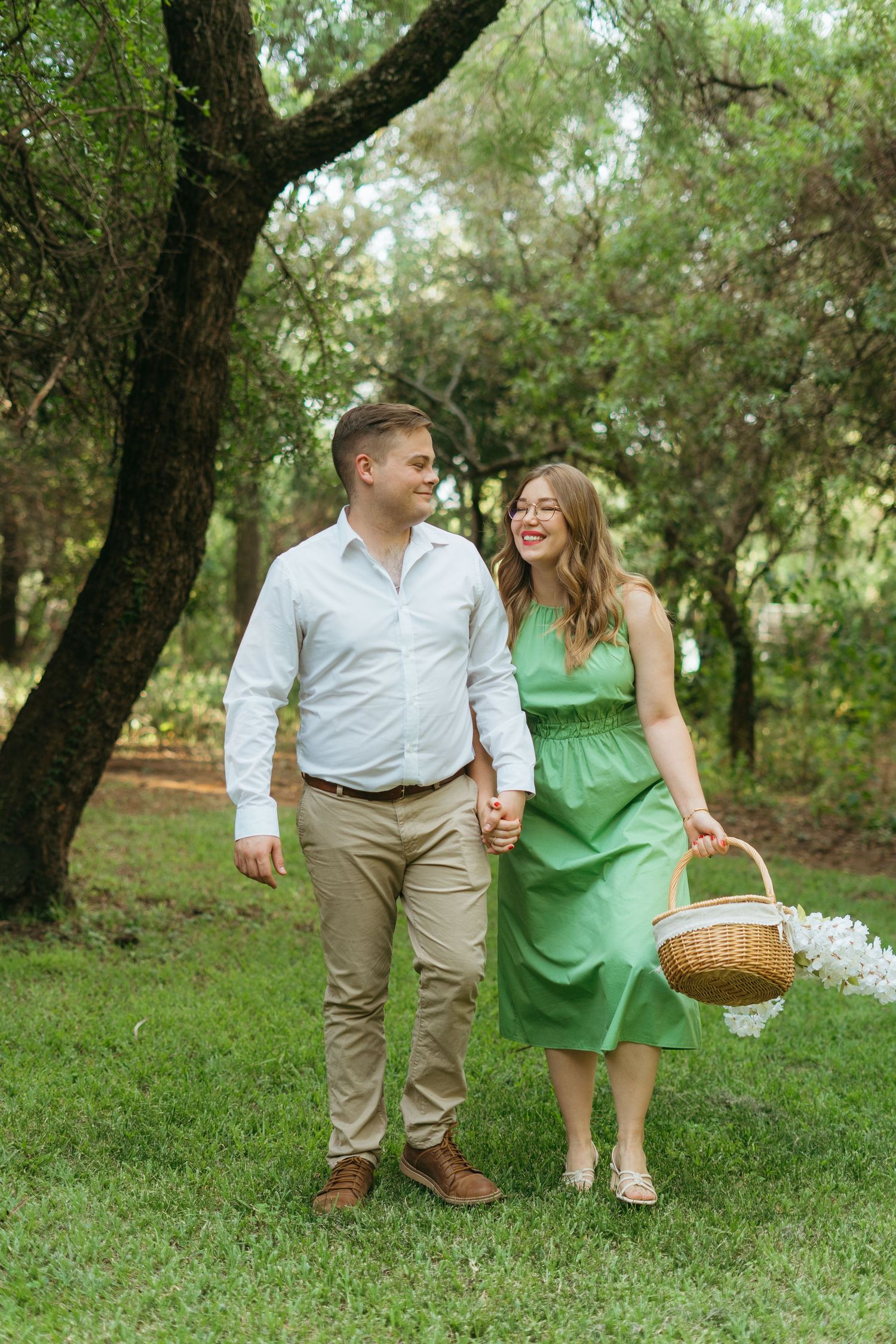 A couple enjoys a romantic stroll in a lush garden setting with a picnic basket on a sunny afternoon.