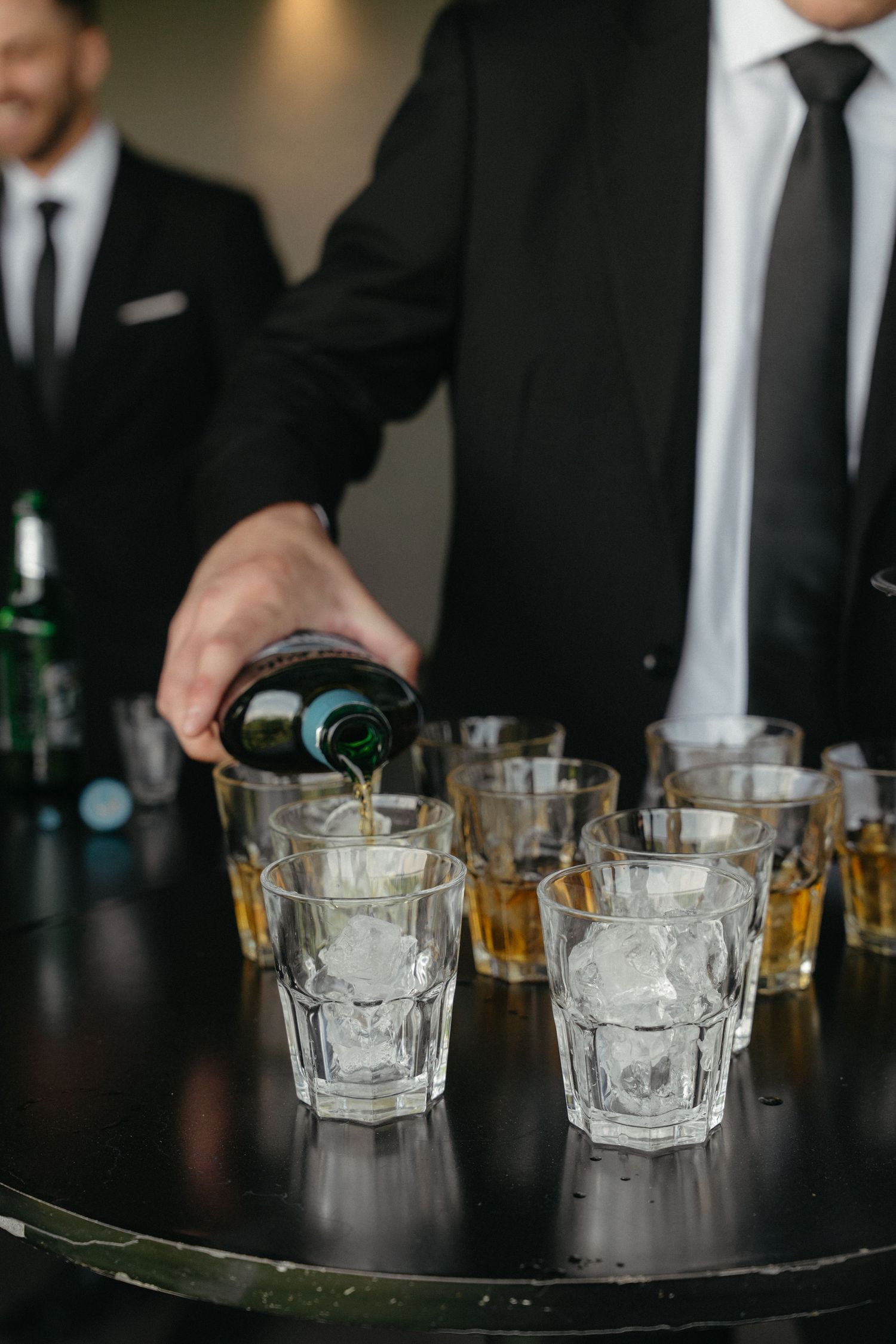 Empty cocktail glasses with ice cubes arranged on a dark bar counter at an elegant event.