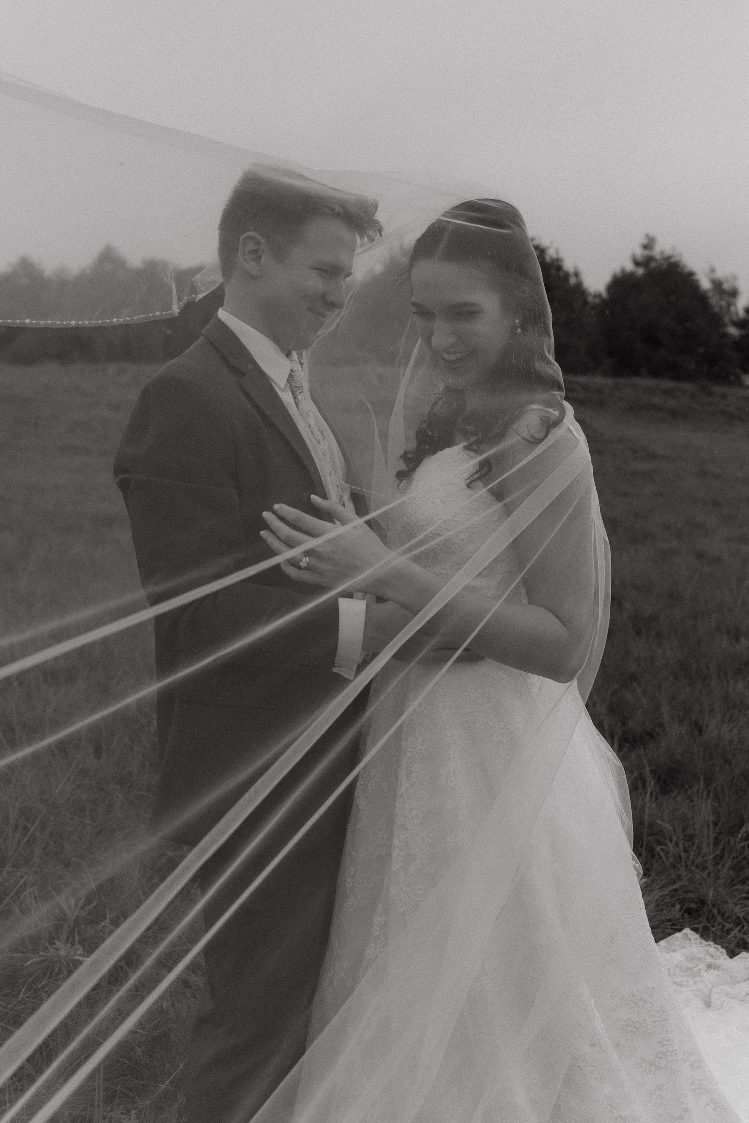 Black and white wedding photo series showing couple kissing through a sheer veil in an outdoor field setting.