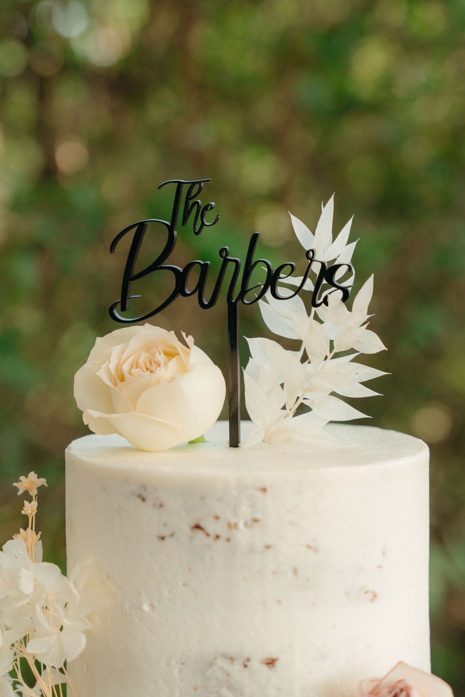 A white wedding cake decorated with delicate white butterflies and peach roses features an elegant black cake topper.