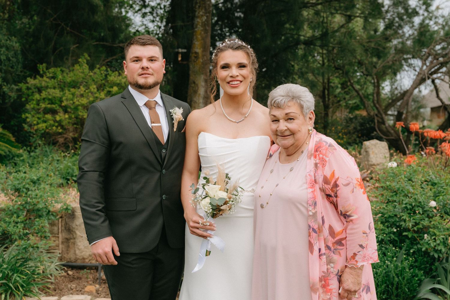 A wedding party poses together in a lush garden setting on a summer day.