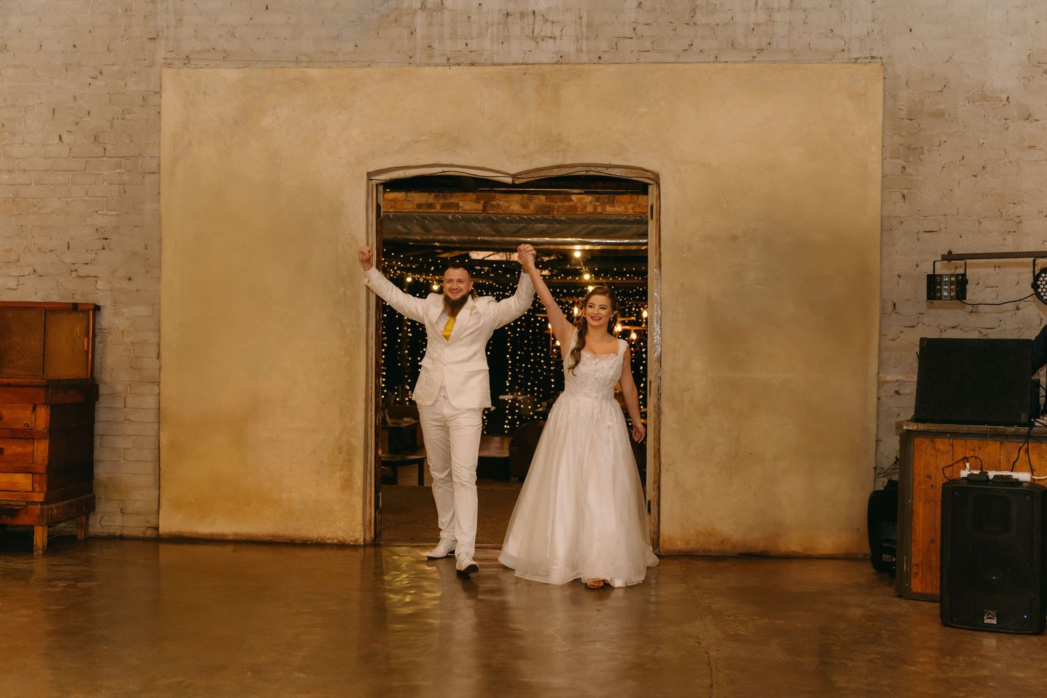 Wedding couple celebrating with raised arms in an industrial venue entrance.