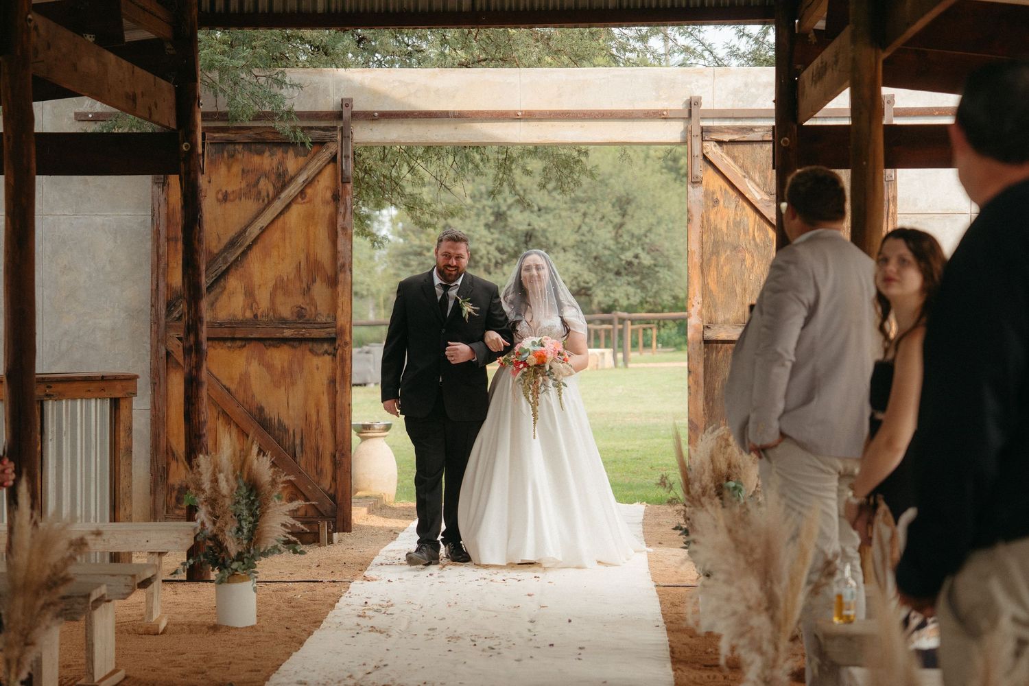 A rustic barn doorway frames a wedding ceremony entrance with wooden beams and natural light.
