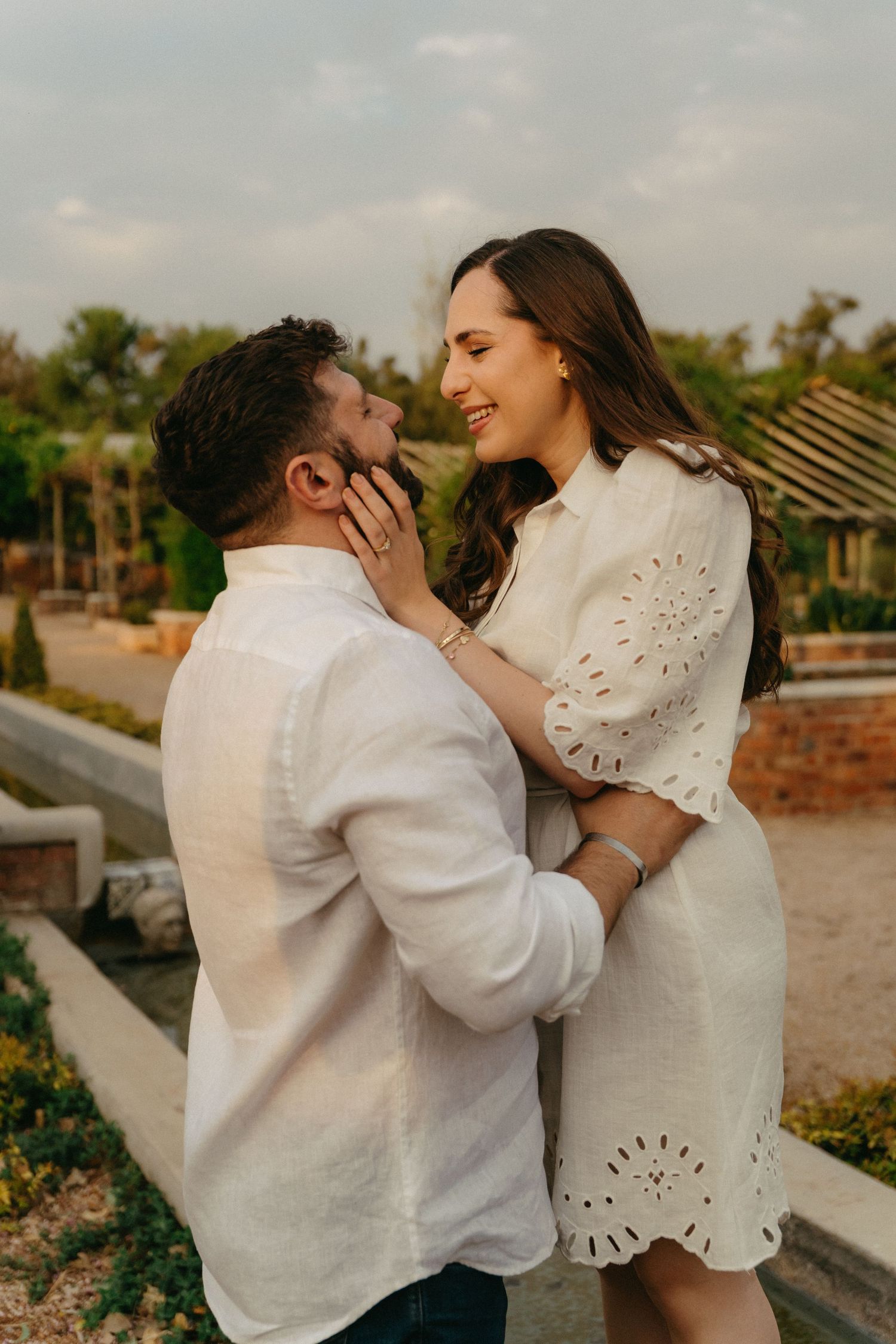 A romantic moment between a couple in white outfits standing in an outdoor garden setting.