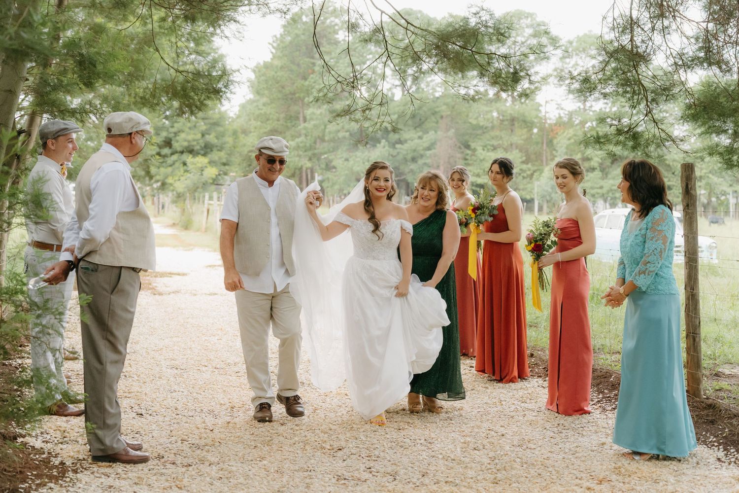 Wedding party walking along wooded path with colorful bridesmaid dresses and white bridal gown.