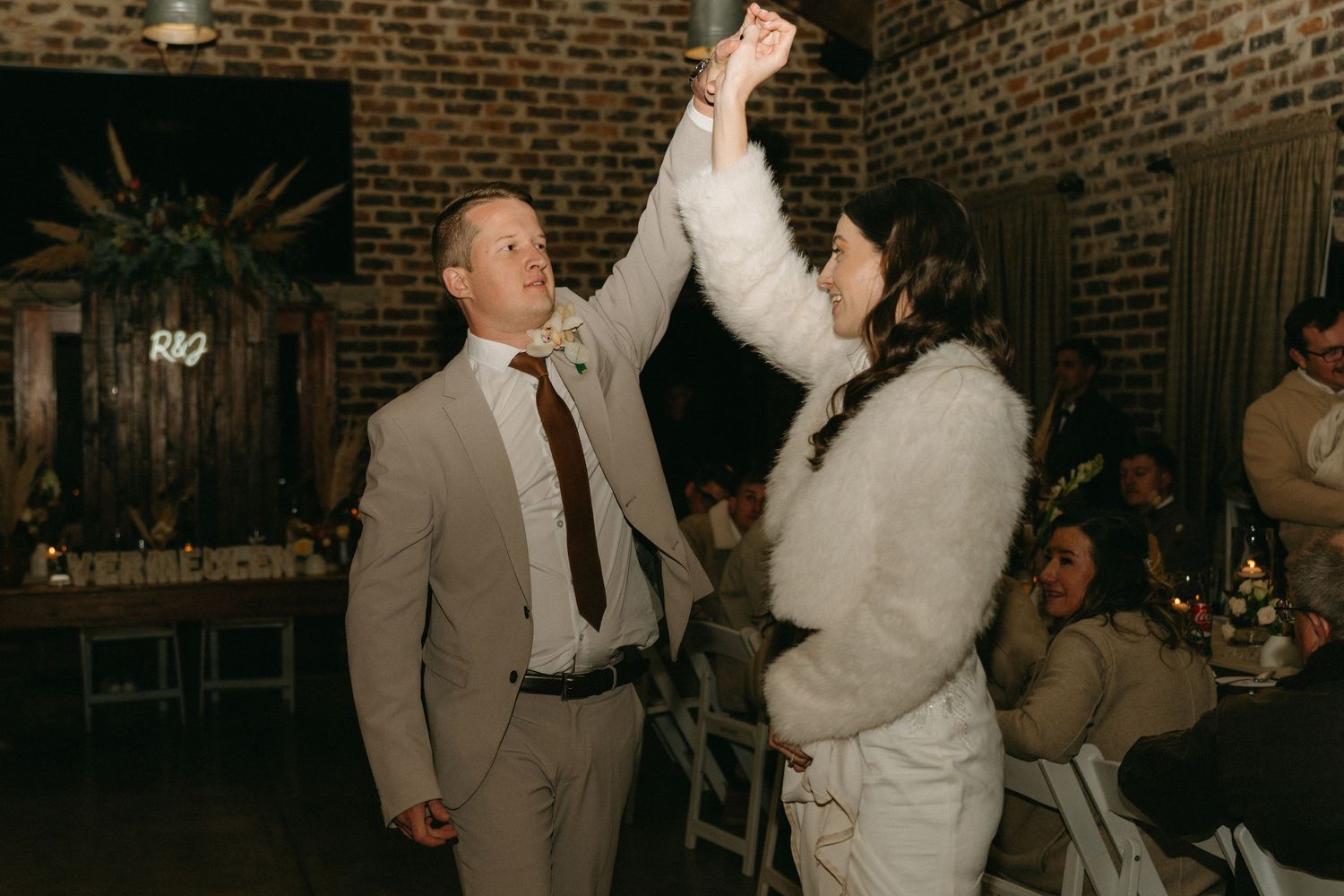 A couple shares their first dance together at a wedding reception in a rustic brick-walled venue.
