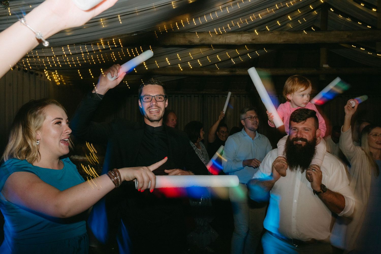 Wedding guests dancing and celebrating on a dimly lit dance floor with string lights overhead.