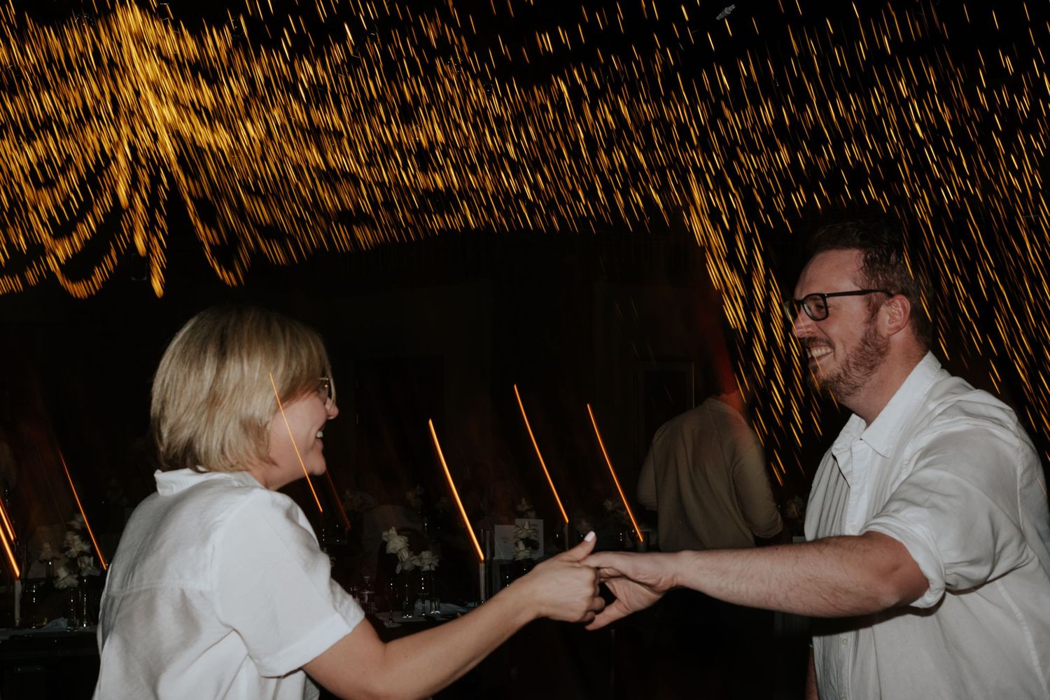 Dancing couples celebrate on the dance floor under golden string lights.