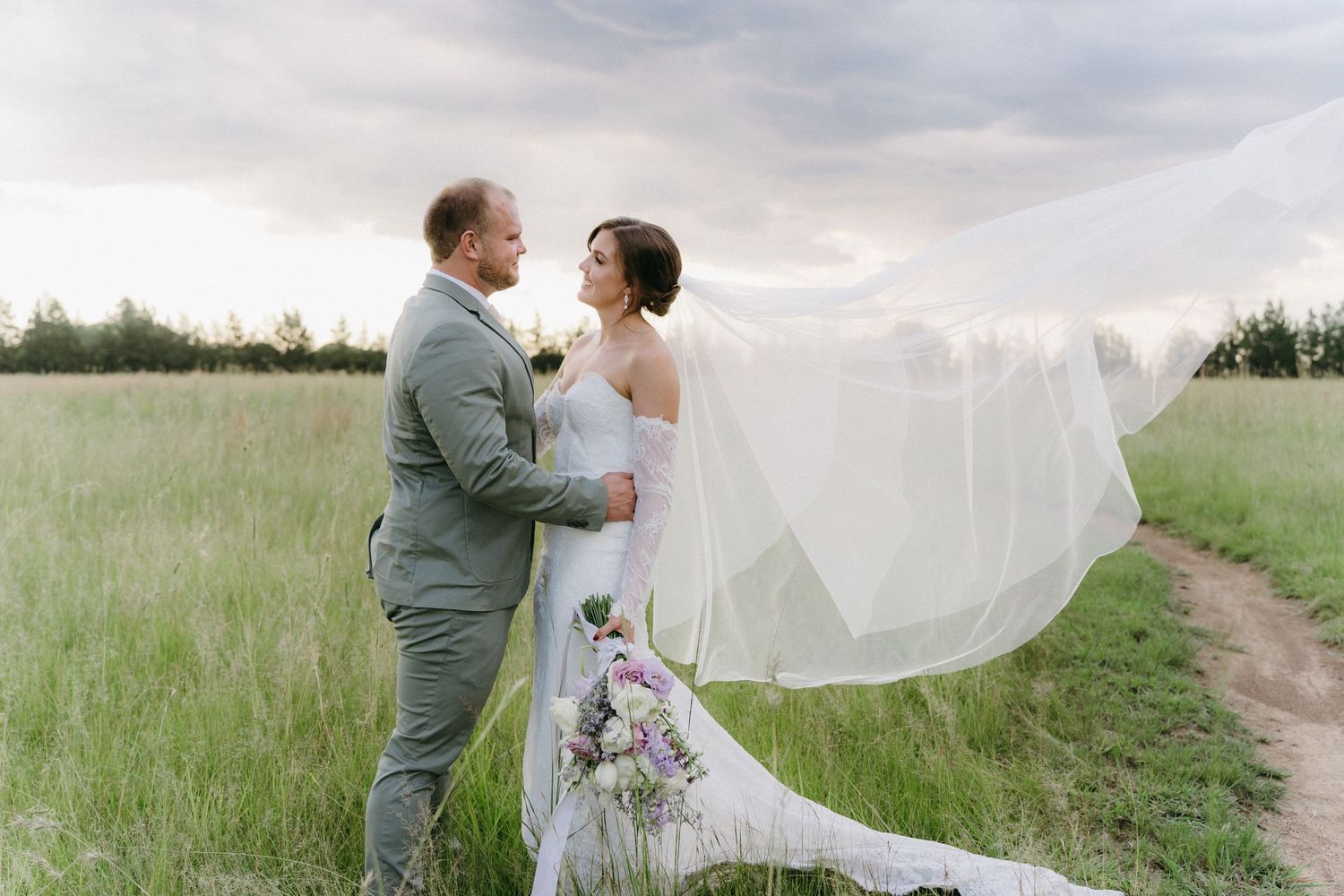 A romantic couple embraces in a meadow as the bride's veil flows dramatically in the breeze.