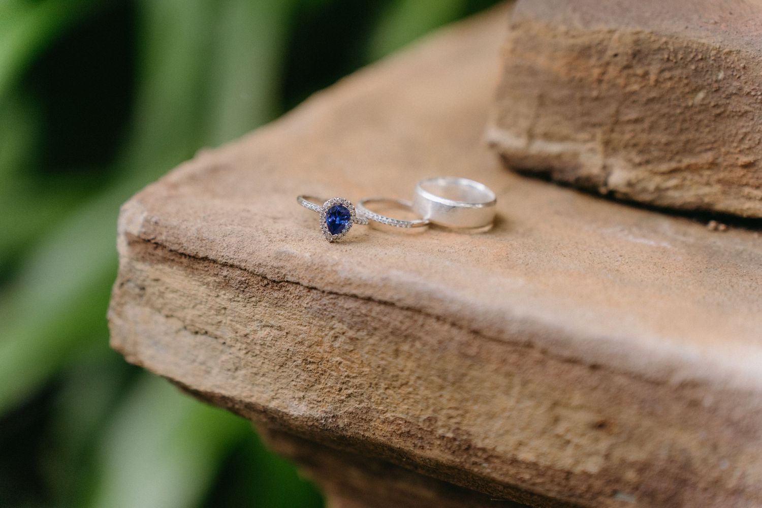 Wedding rings with a blue sapphire detail rest on a weathered stone surface.