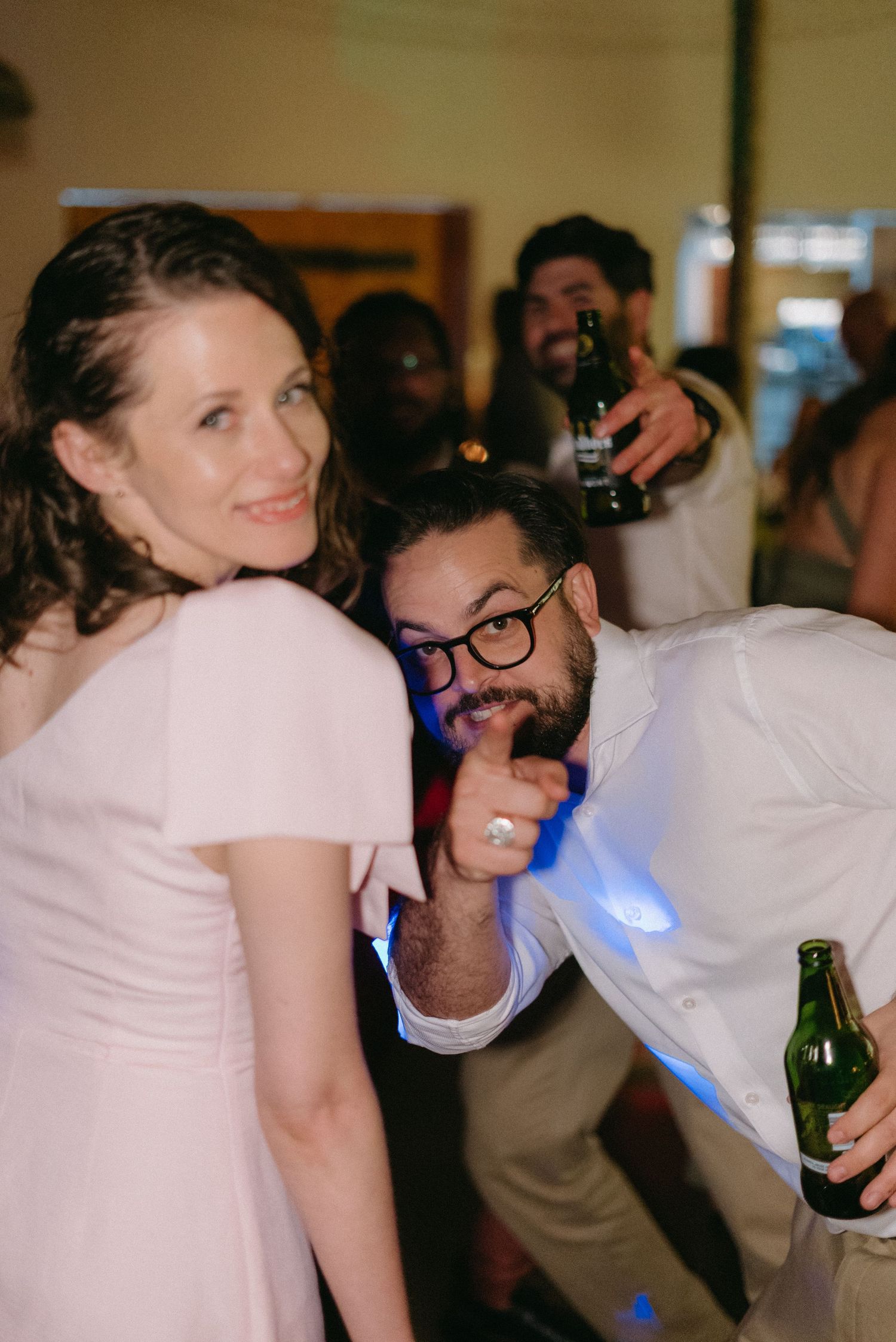 Indoor reception celebration with guests dancing and holding drinks under dim lighting.