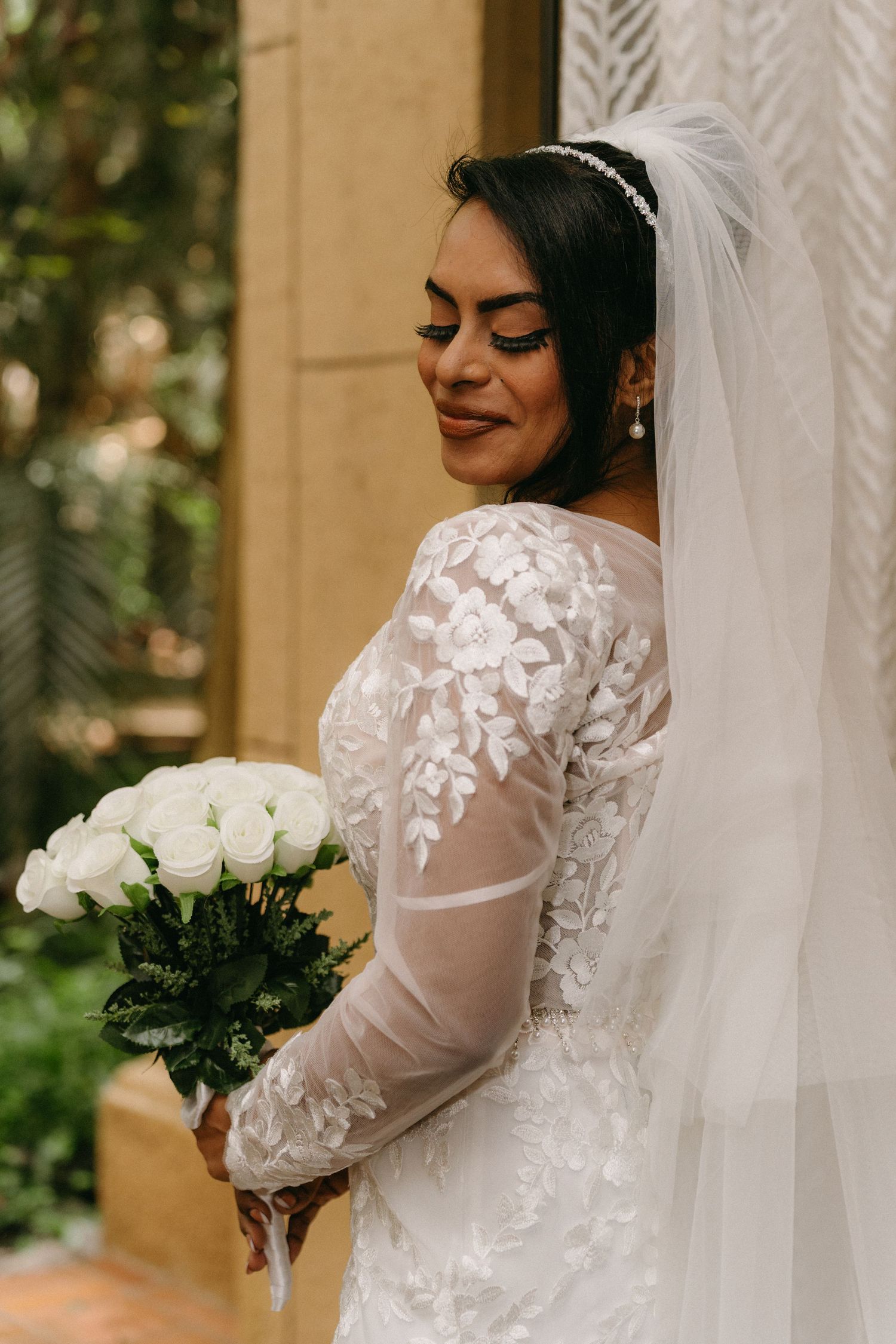 Beautiful bride in a lace and sheer white wedding dress with veil holding a bouquet of white roses.