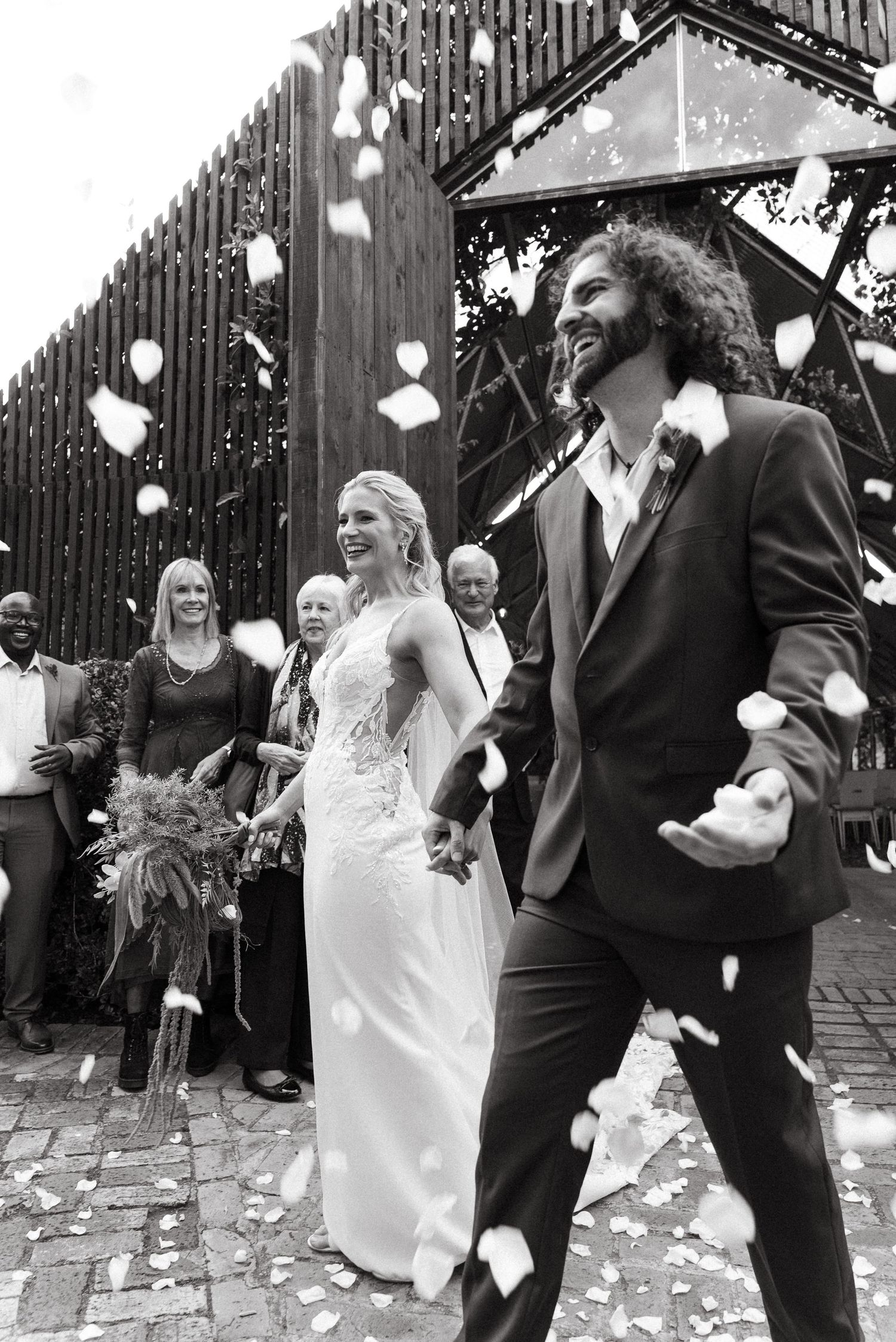 Black and white photo of a joyful newlywed couple walking through confetti after their wedding ceremony.