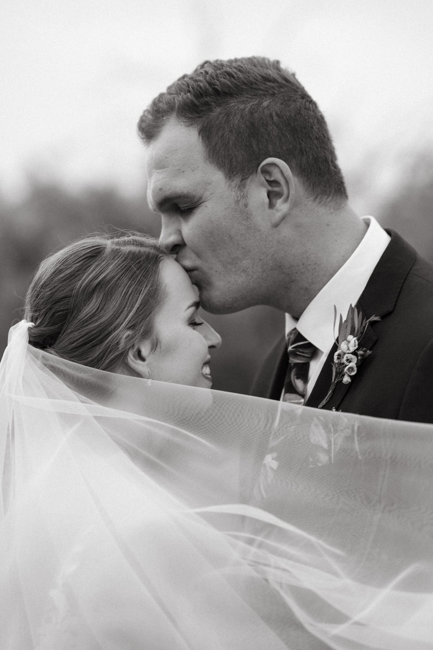 Black and white photo of bride and groom sharing a kiss in Dinokeng beneath flowing wedding veil.