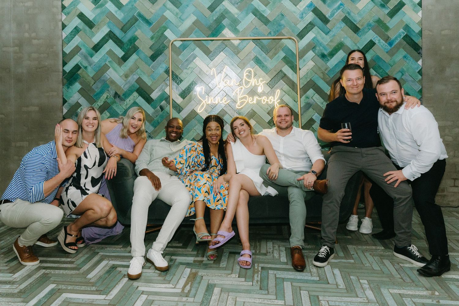 A group of people sitting together on benches against a teal chevron patterned wall.