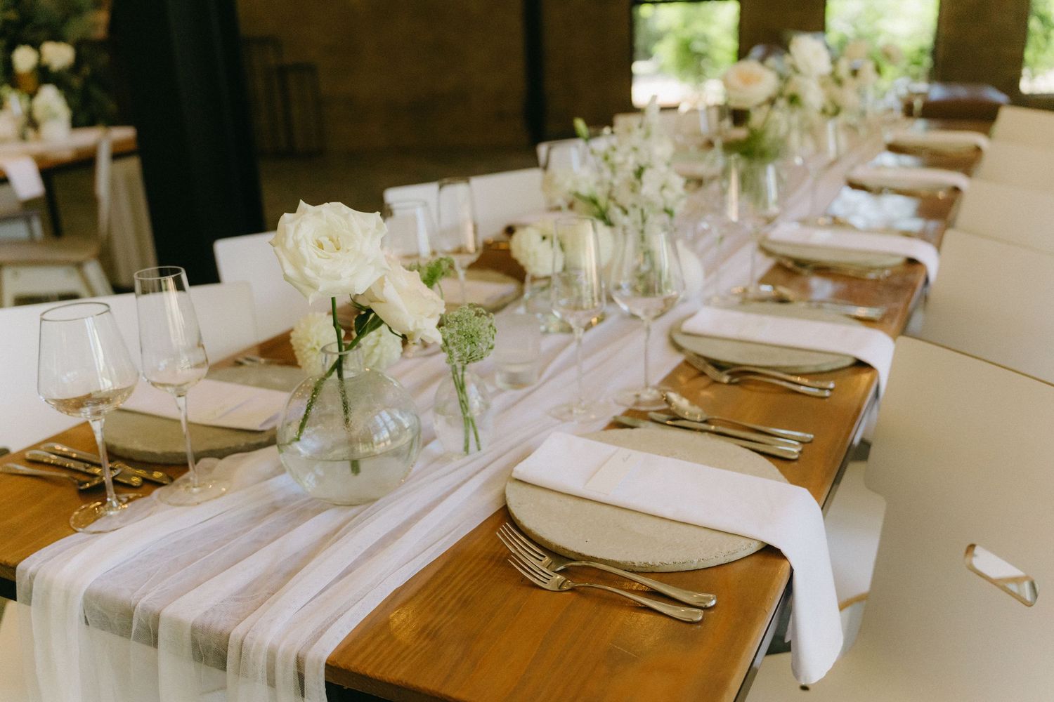 An elegant wedding table setting with white linens, wooden plates, and delicate floral centerpieces in glass vases.