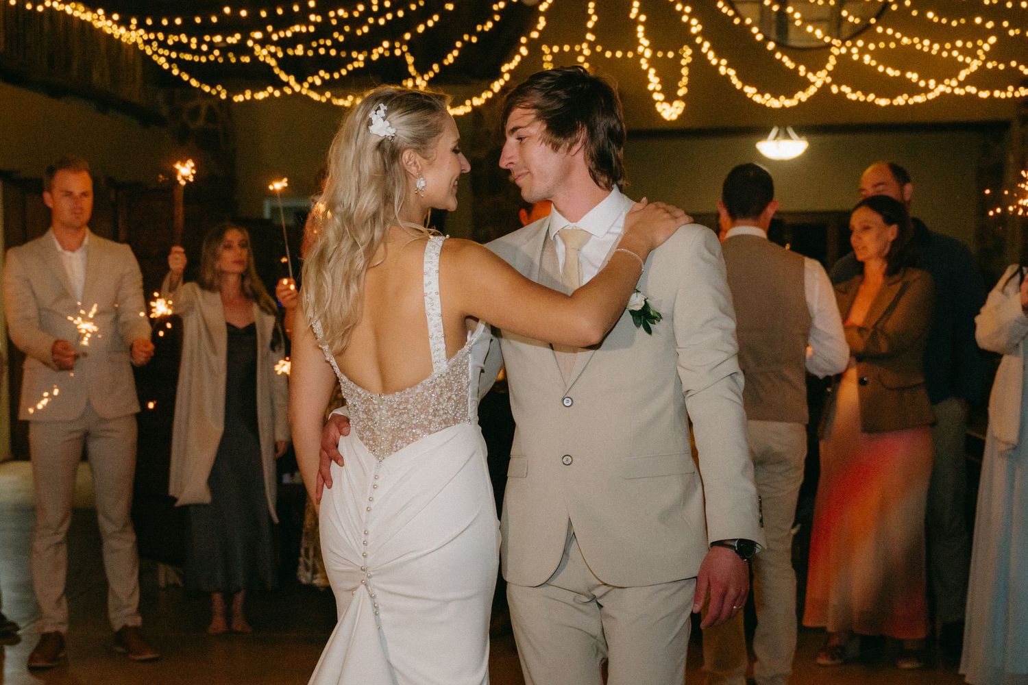 Wedding reception dance floor glows under golden string light canopy as guests celebrate.