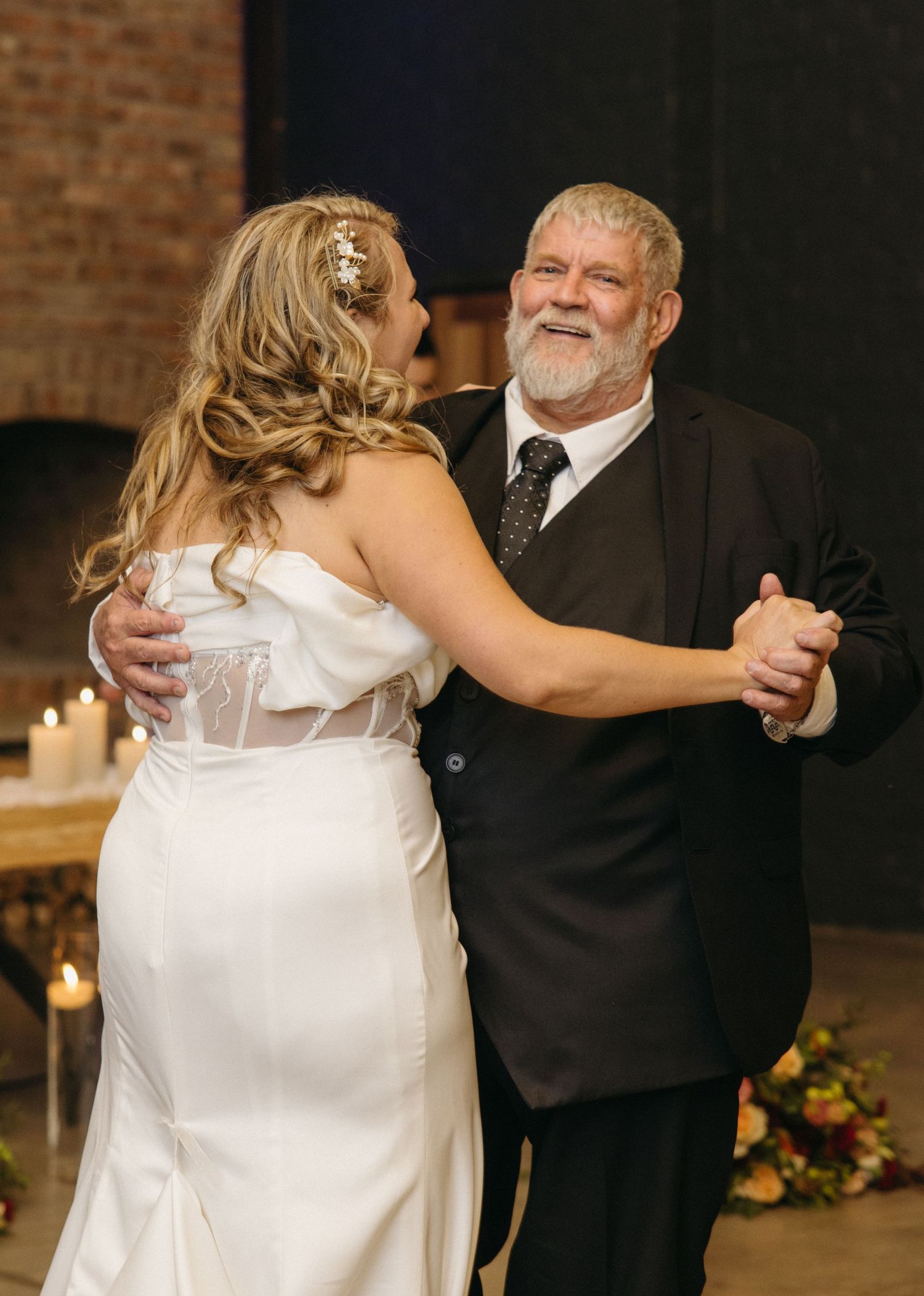 Special dance moment shared between wedding guests in candlelit venue with brick walls.