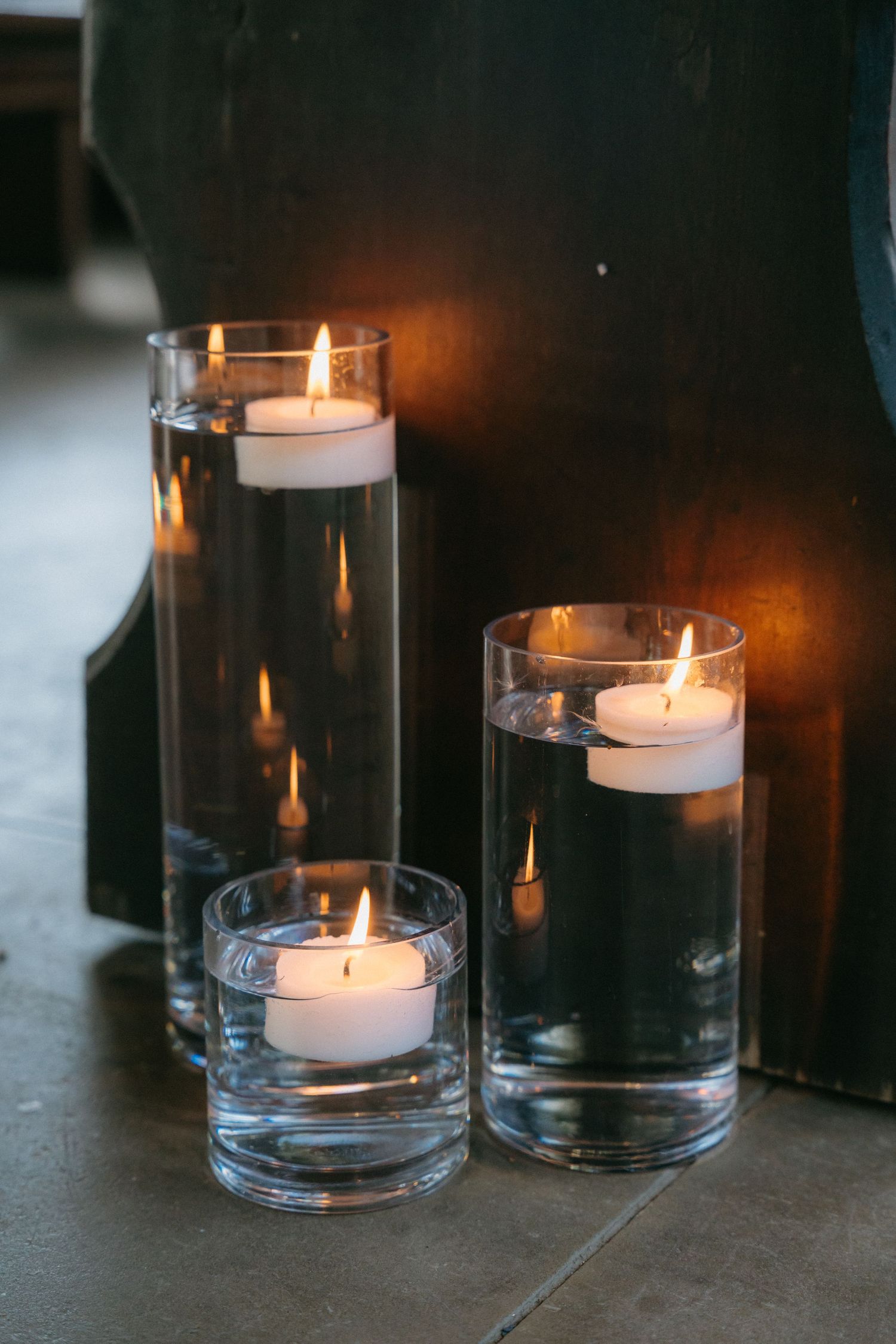 Glass cylinder vases with floating candles create an elegant ambiance against a dark background.