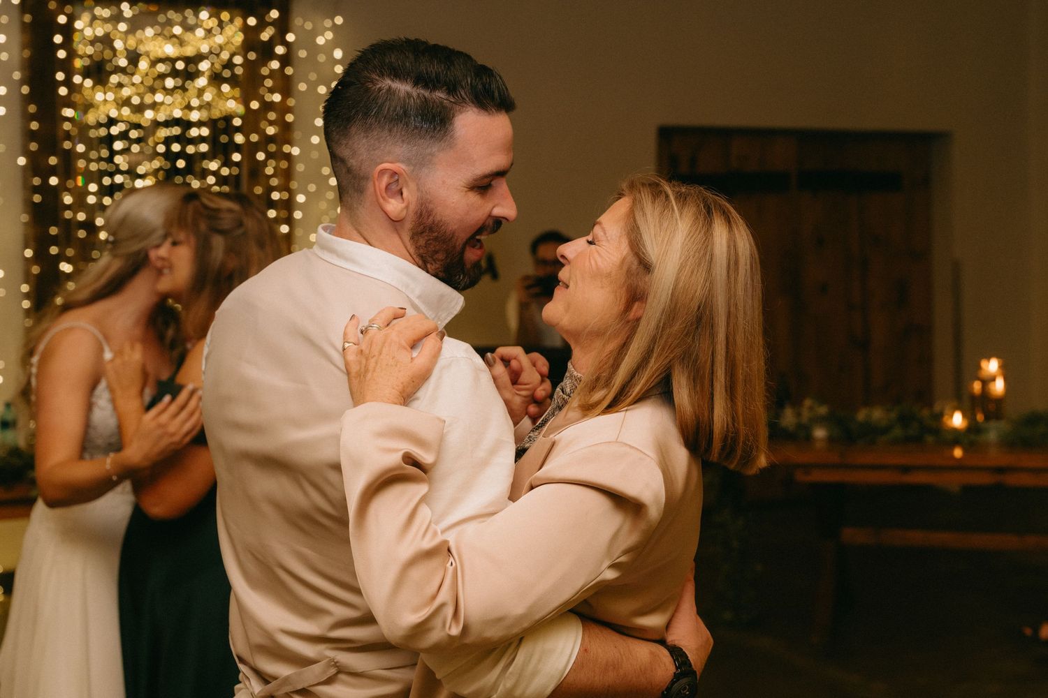 A couple shares an intimate dance moment under warm string lights at their wedding reception.