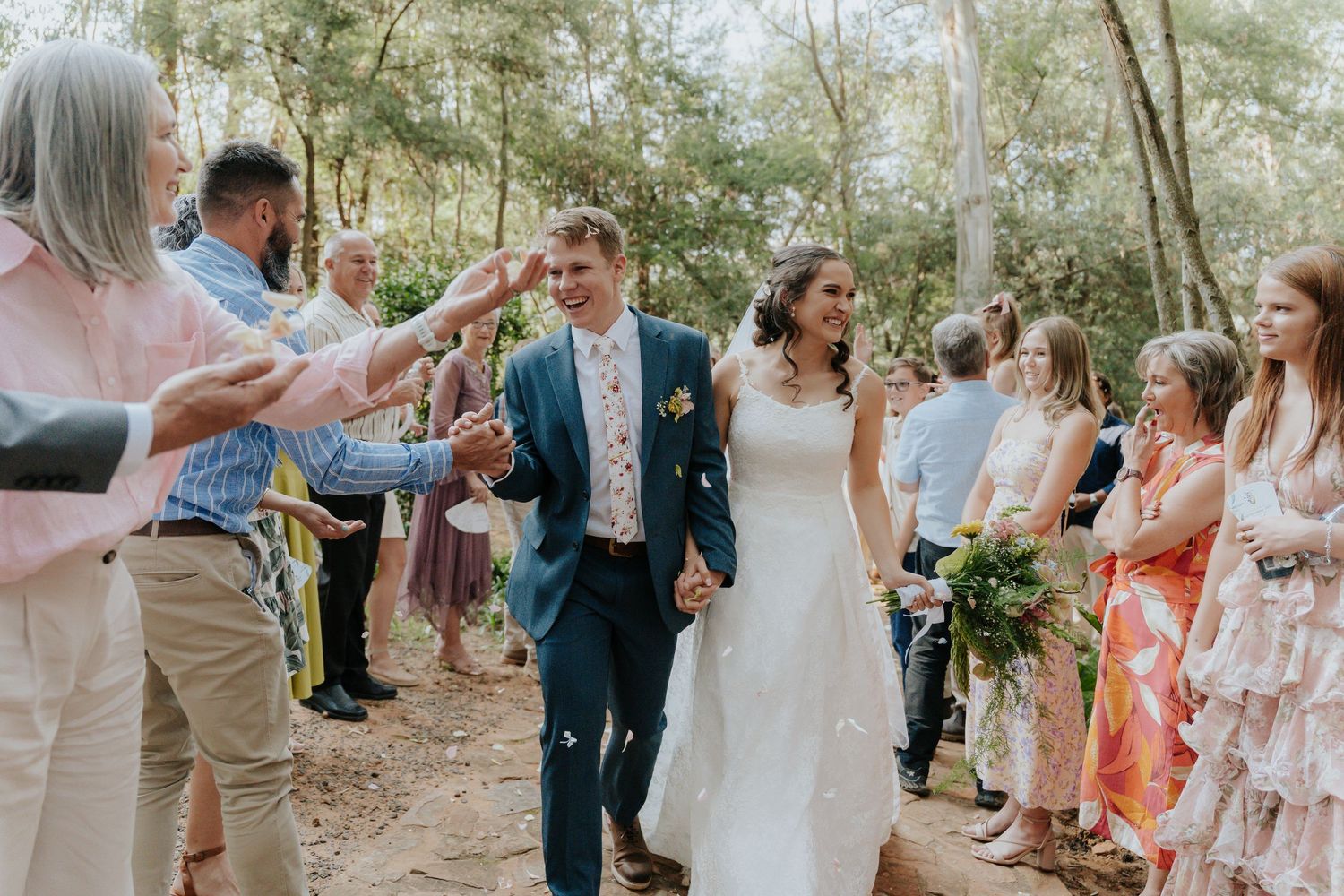 Wedding guests dance and celebrate together in a lush outdoor garden setting during a joyful reception party.