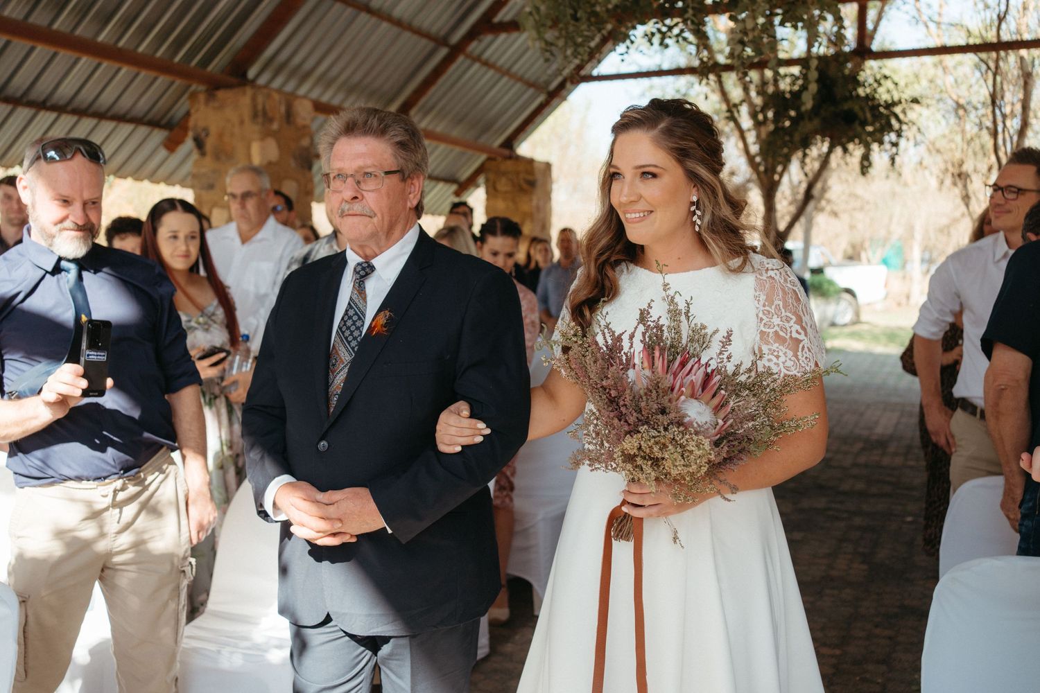 An outdoor wedding ceremony under a covered area with rustic decor.