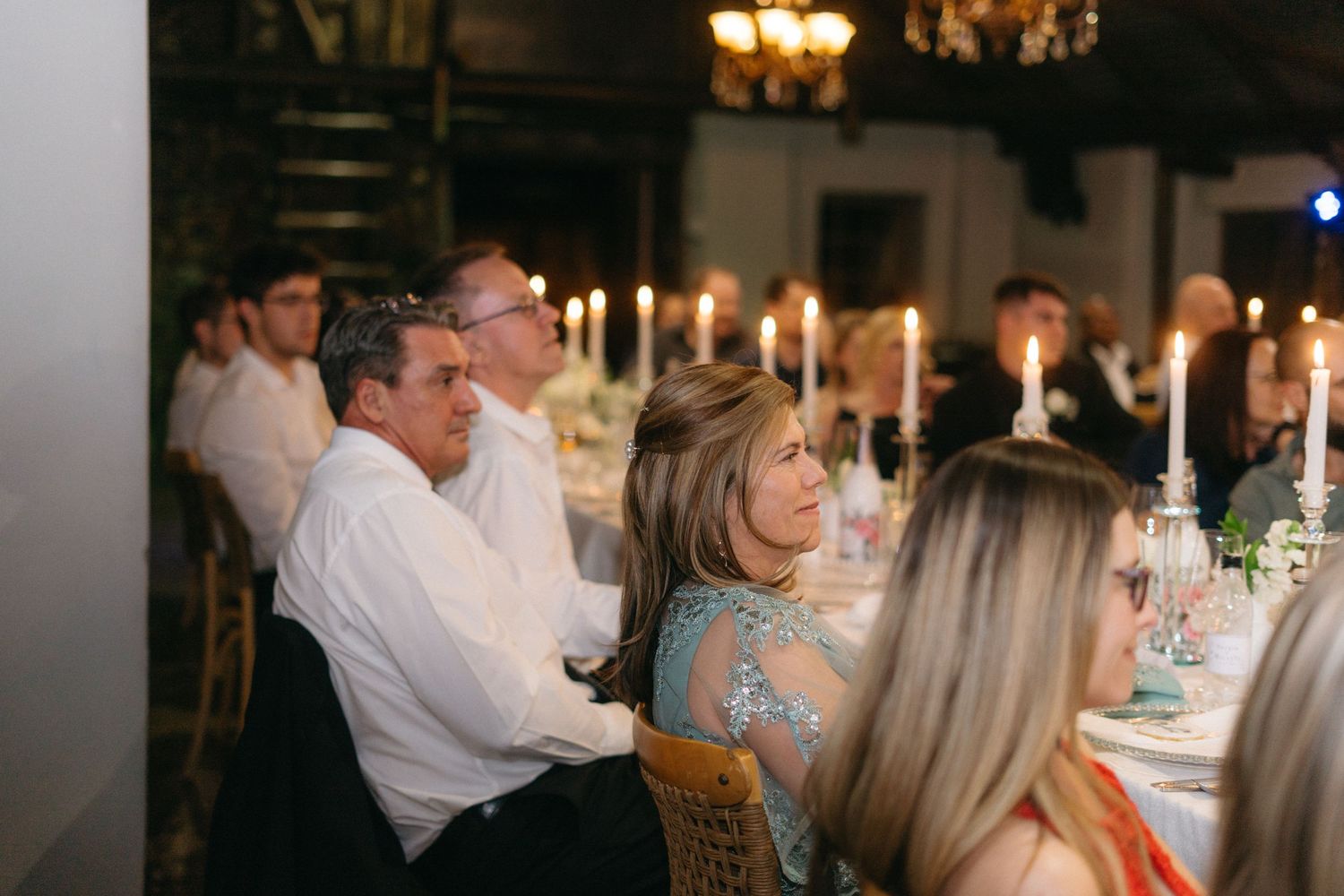 People enjoying an elegant candlelit dinner party at a dimly lit venue with chandeliers.