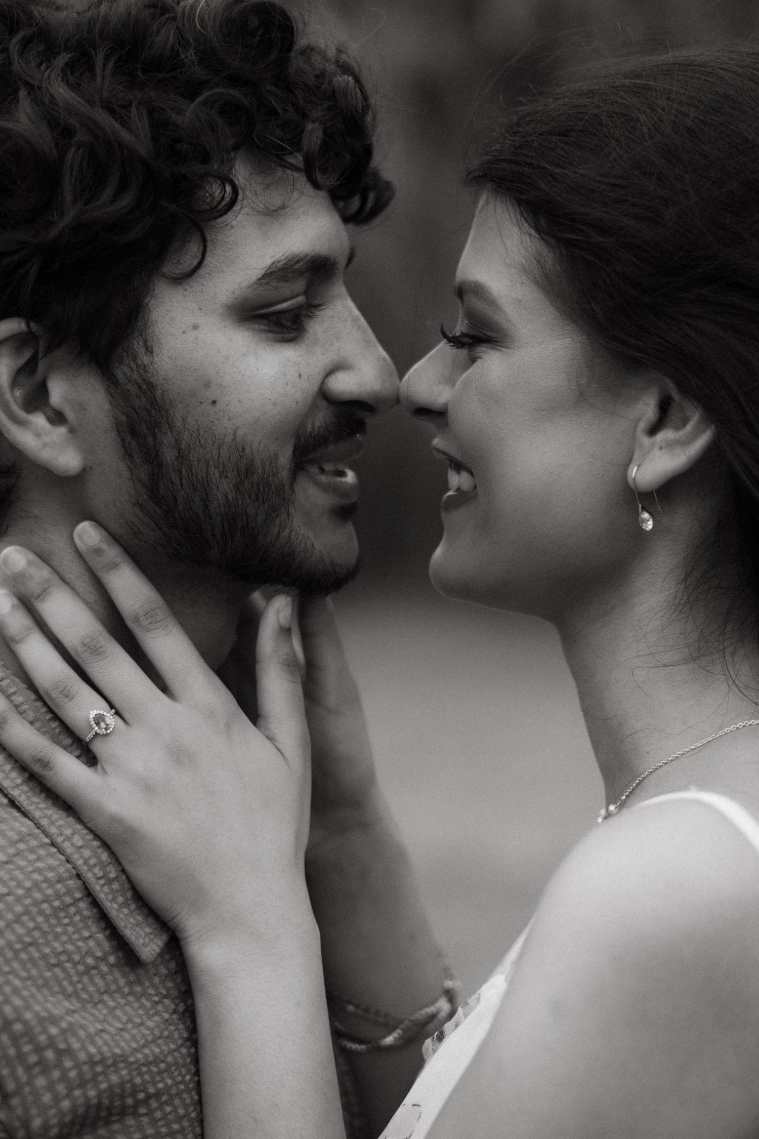 A romantic black and white close-up portrait of a couple sharing an intimate moment with gentle smiles.