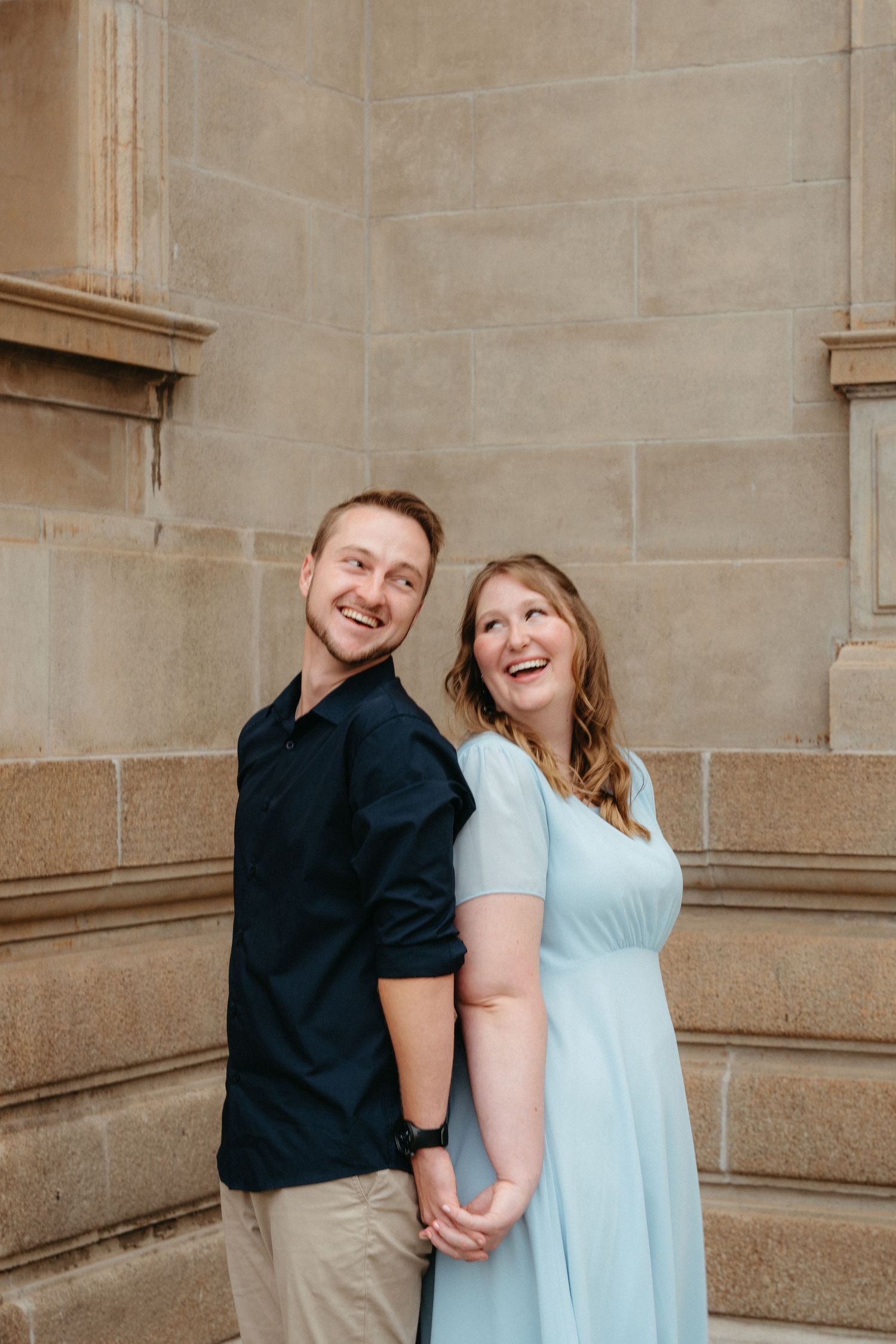A couple shares a joyful moment together against a stone wall background during an engagement photo session.