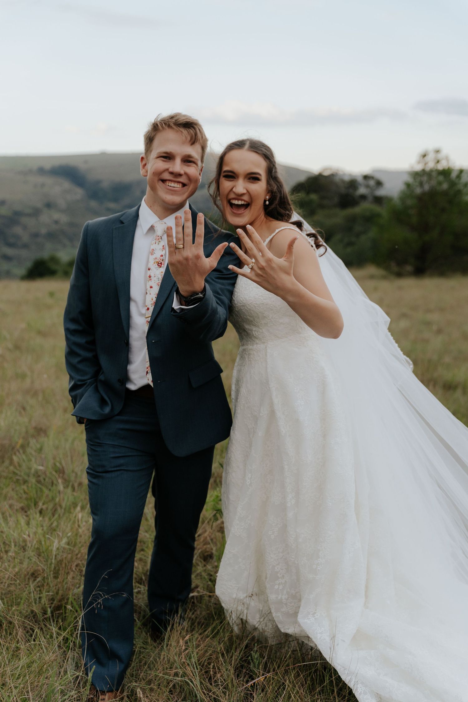 A happy couple in wedding attire share joyful moments together in a grassy field during their outdoor wedding photoshoot.