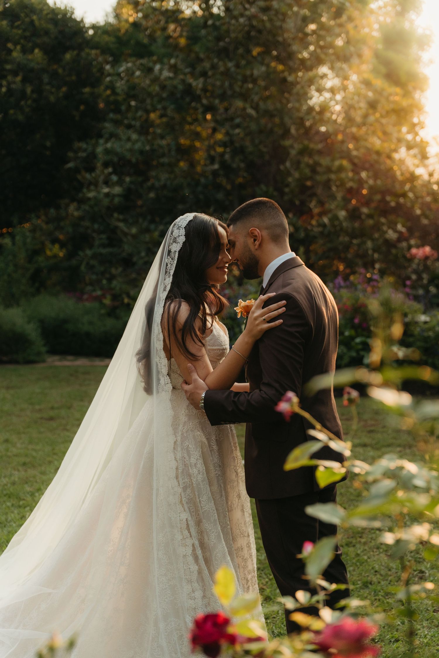 Bride and groom share an intimate moment in a sunlit Beechwood Gardens, South Africa, with her lace veil flowing gracefully.