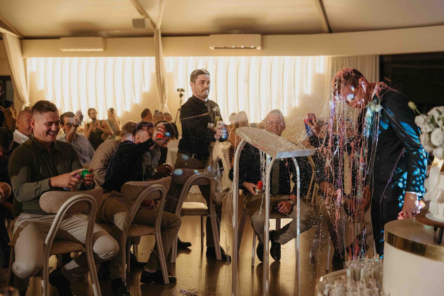 Guests laughing and celebrating at an indoor party with colorful streamers and festive decorations.